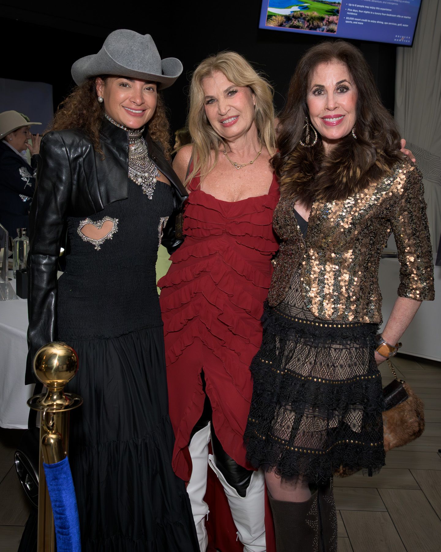 Three women pose together at western-themed charity gala event.