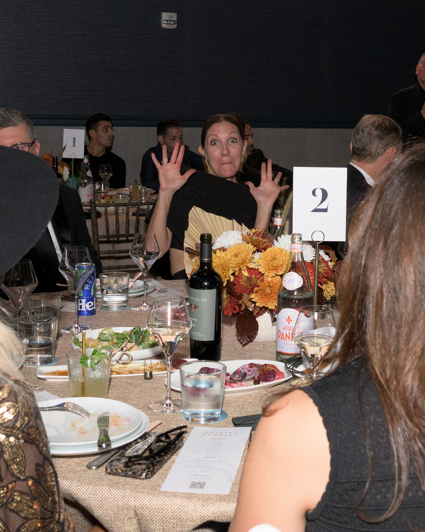 Woman raising hands expressively at table number two during a formal dinner event.