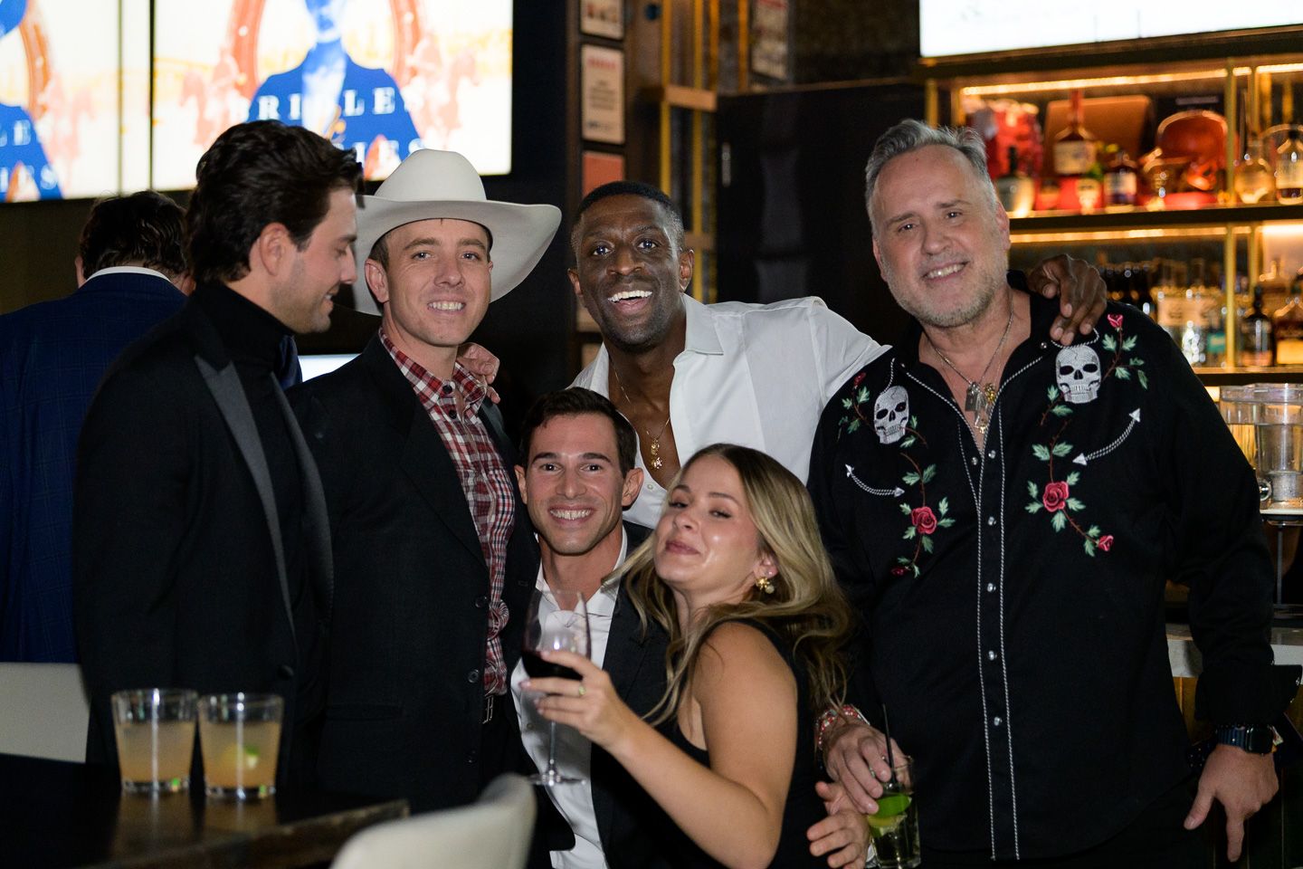 A group of six people smile and pose together at a bar during a social event.