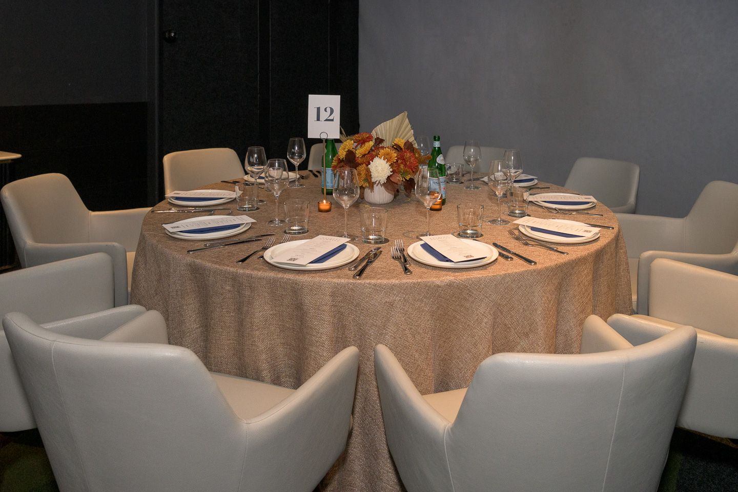 Elegantly set round dining table with floral centerpiece and white chairs at a formal event.