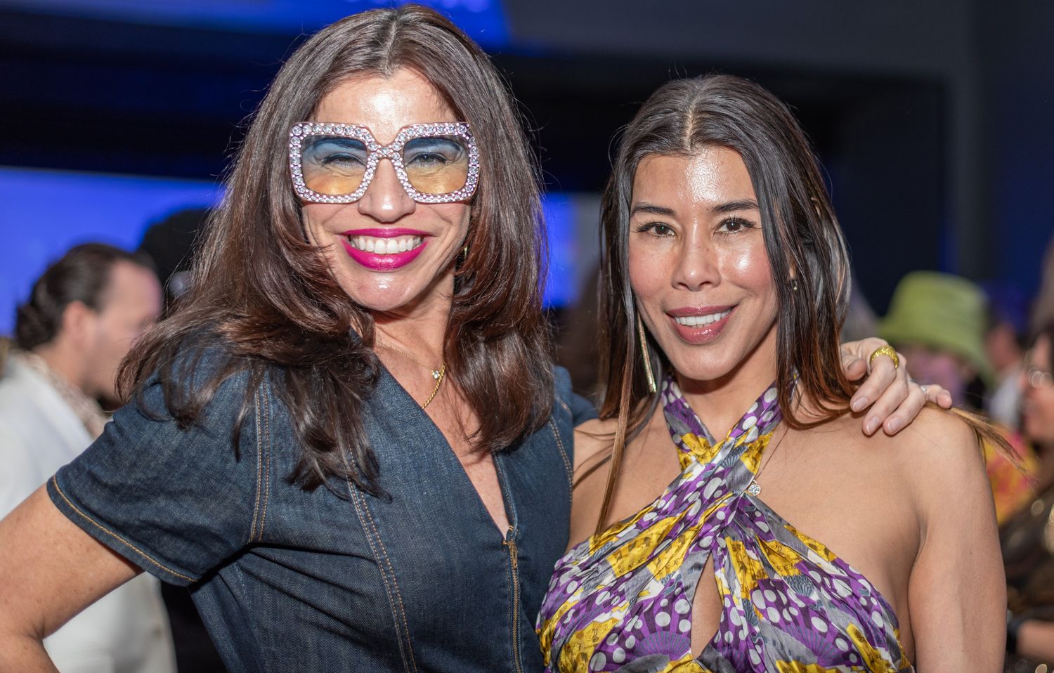 Two women posing together, one wearing decorative sunglasses and colorful dress.