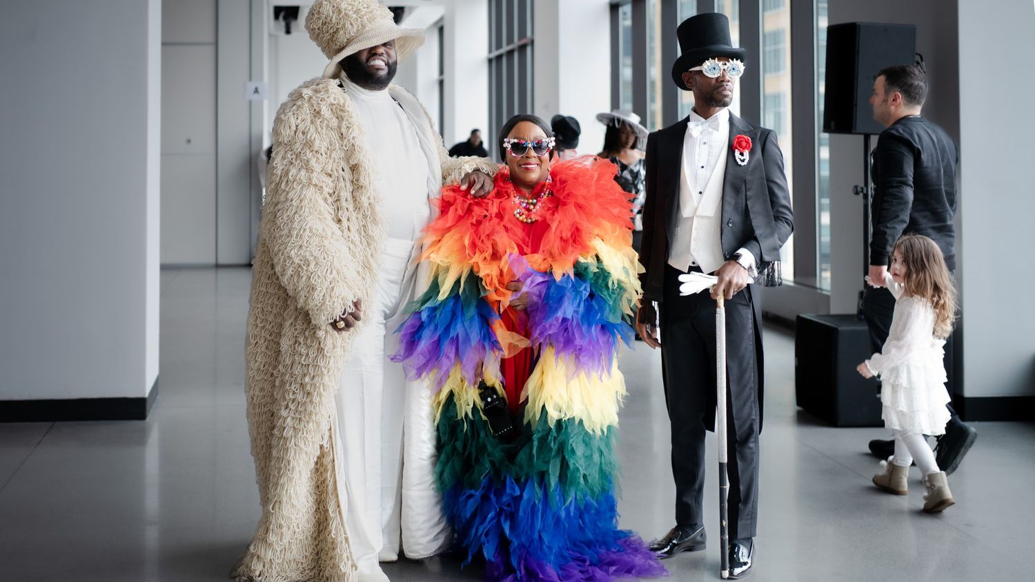 Guests in vibrant costumes including rainbow feathers and bear suit at formal event.