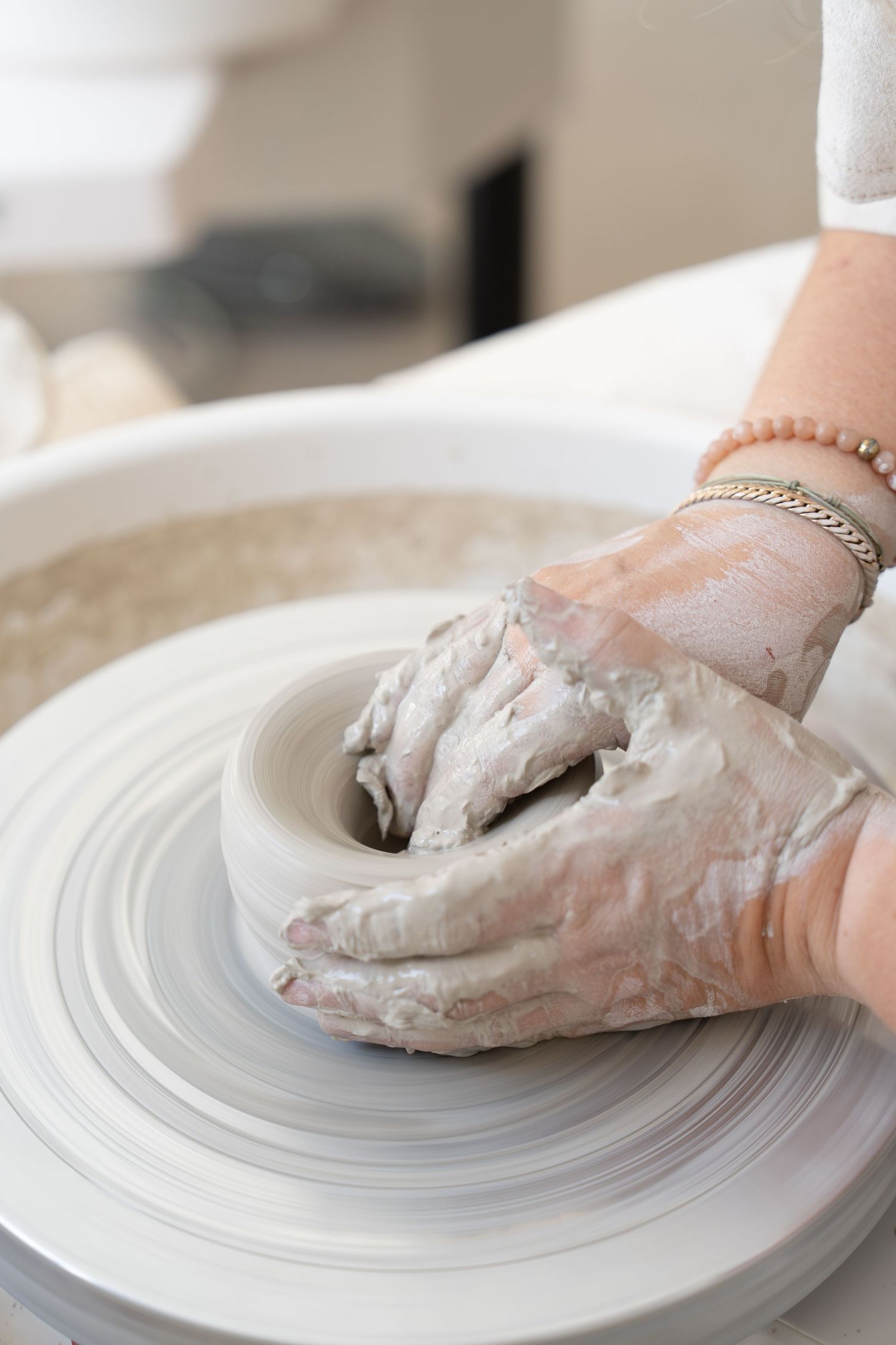 Hands working with clay on pottery wheel creating ceramic vessel.