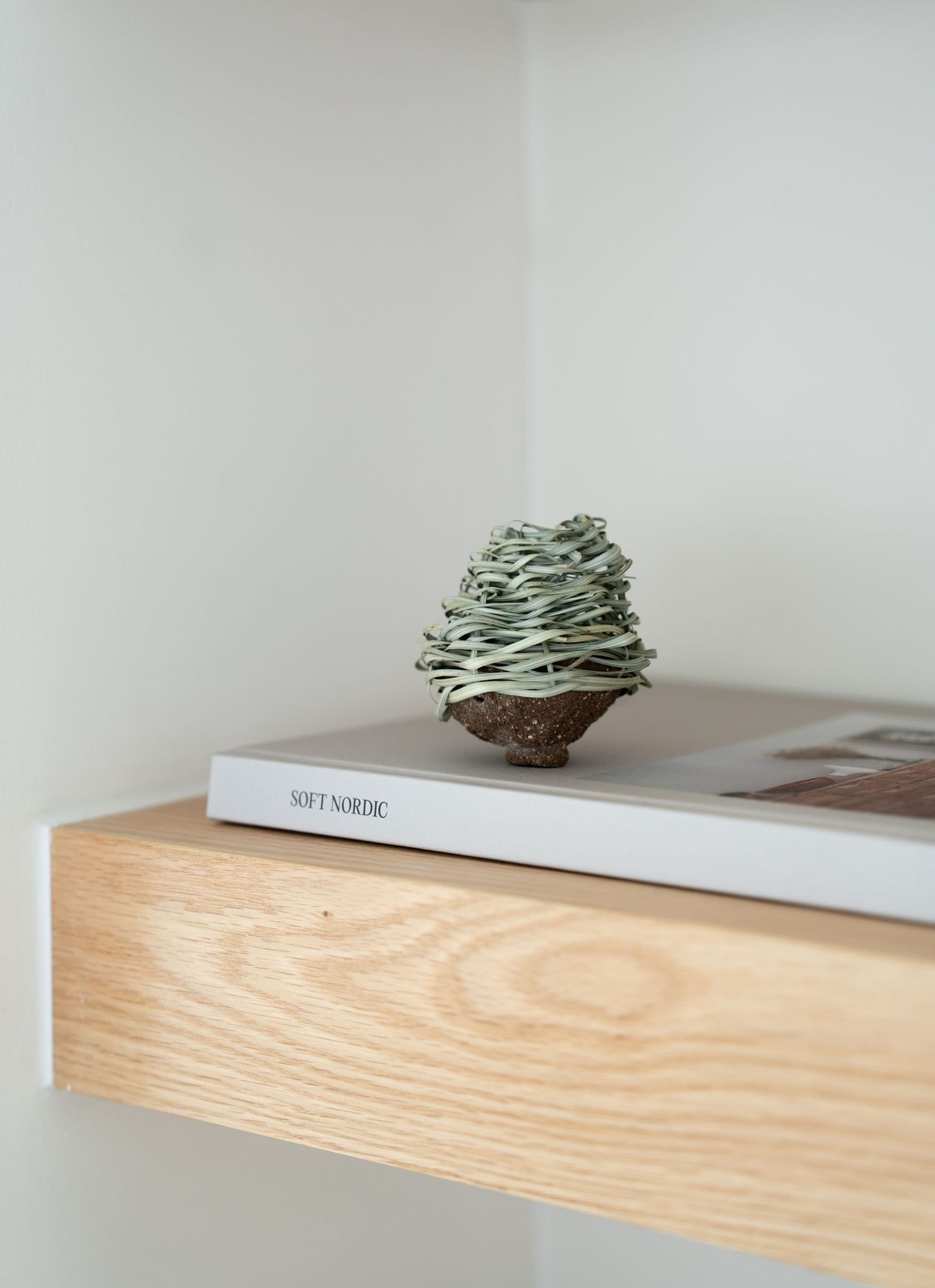 A minimalist wooden floating shelf mounted on a white wall displays a small decorative nest-like object.