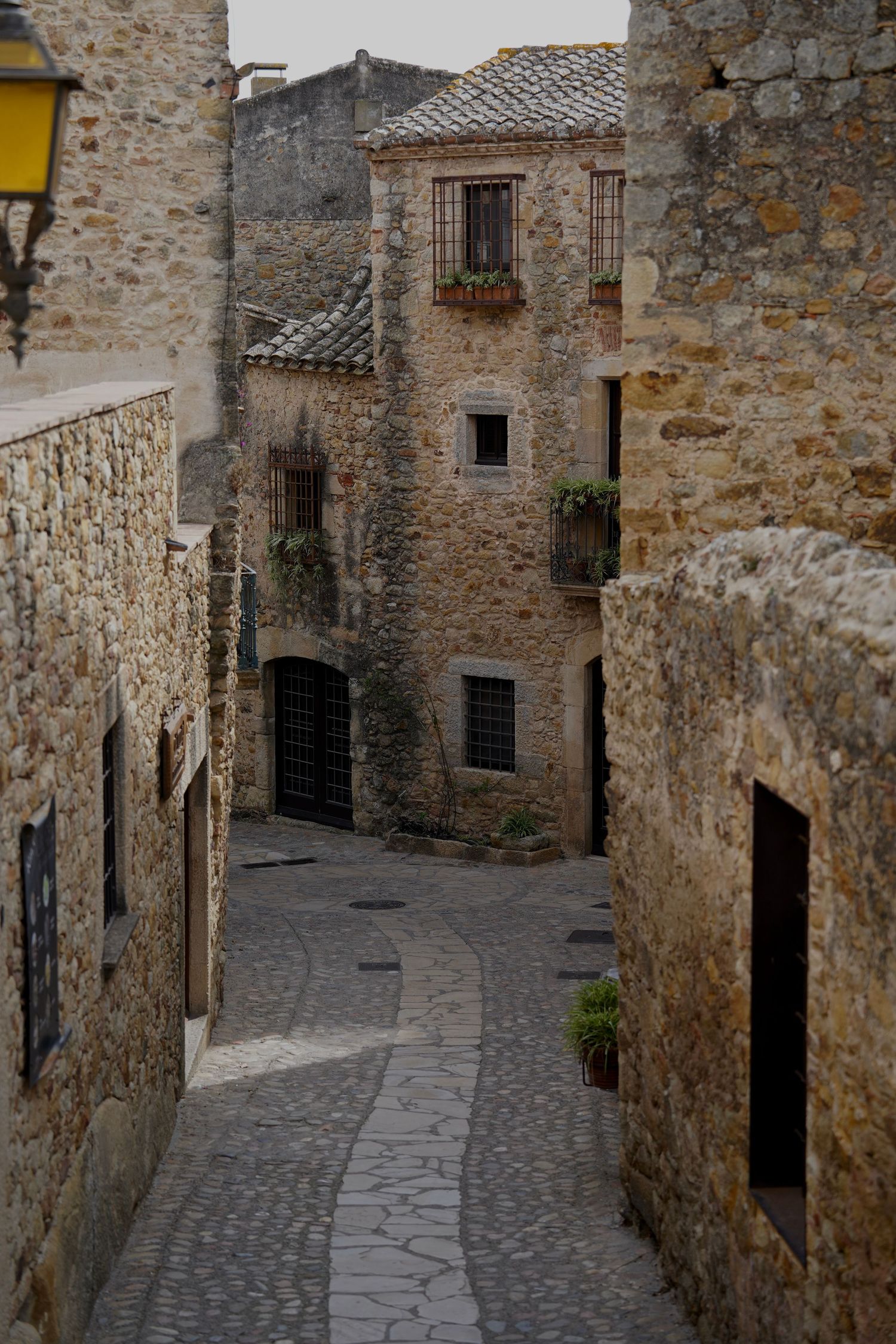 Narrow cobblestone street winding through historic medieval stone buildings in a Mediterranean village.