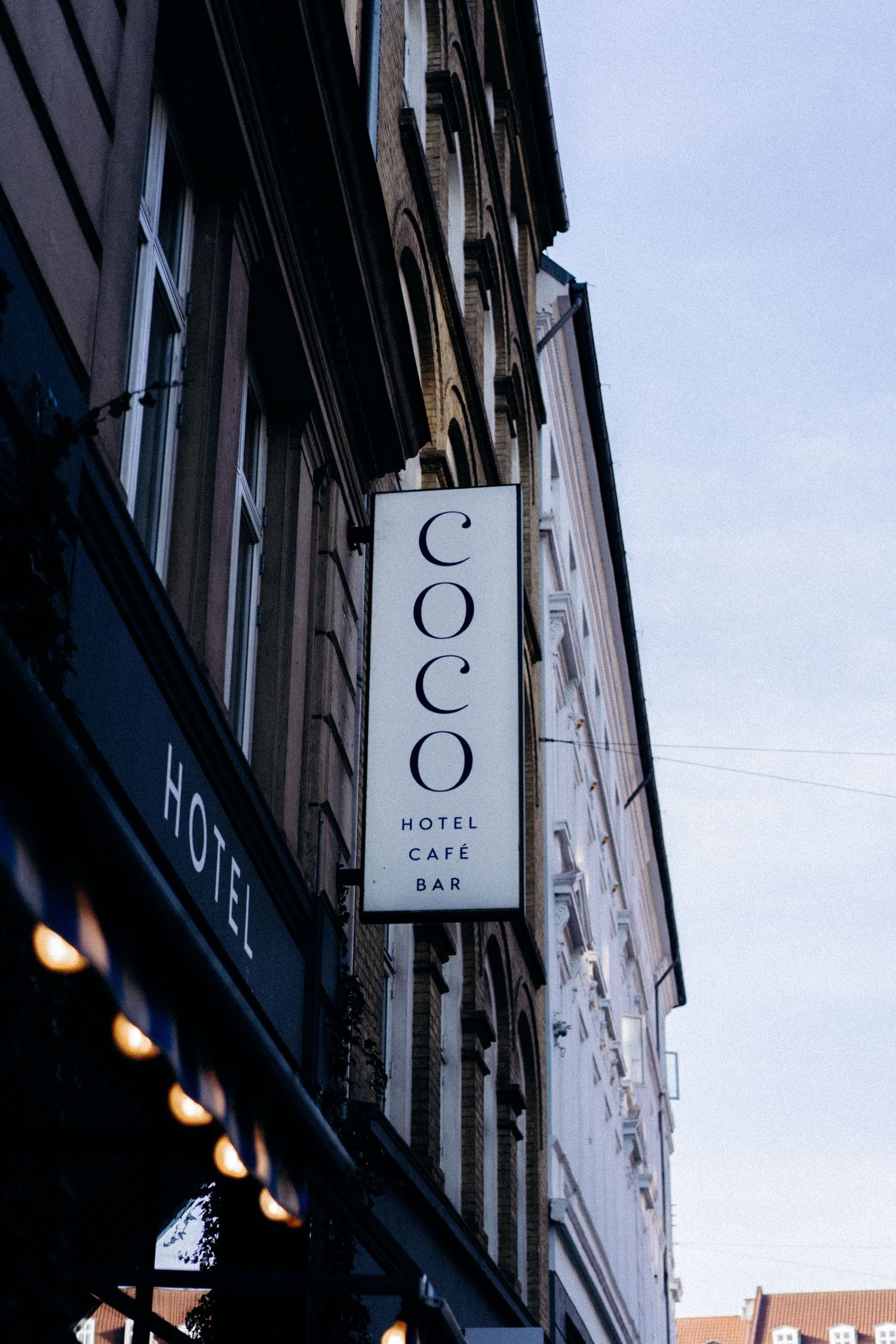 Vertical sign for Coco hotel cafe bar mounted on classic building facade.