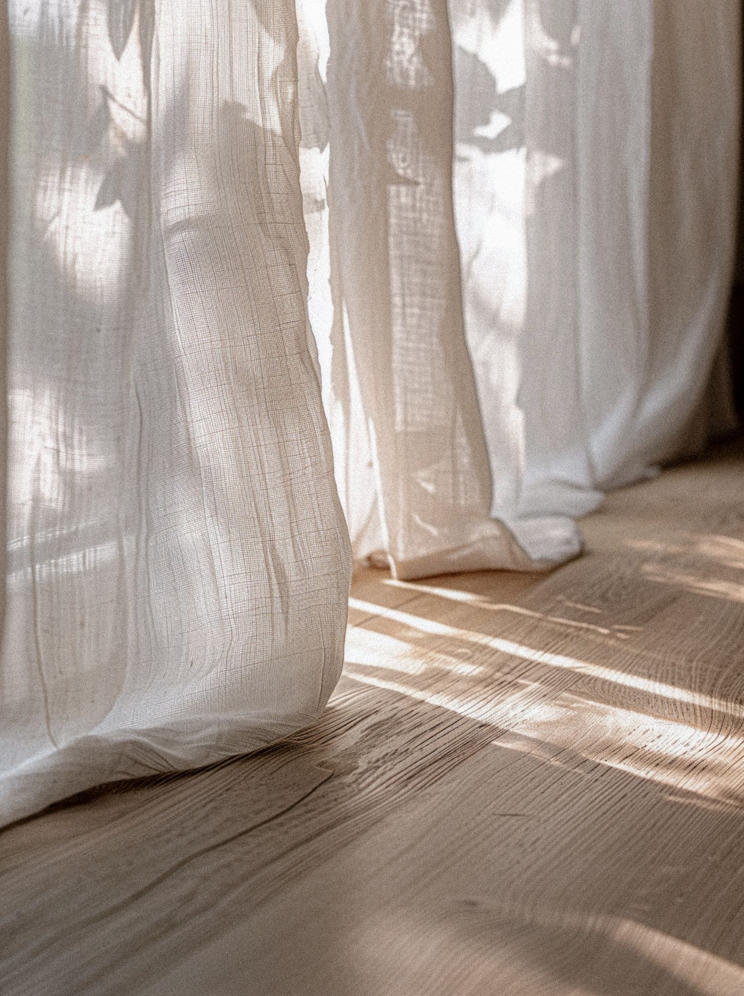 Sunlight streaming through white sheer curtains onto wooden floor.