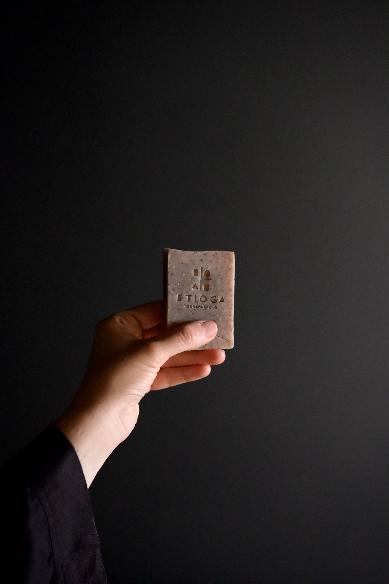 Hand holding a brown bar of soap against a dark background.