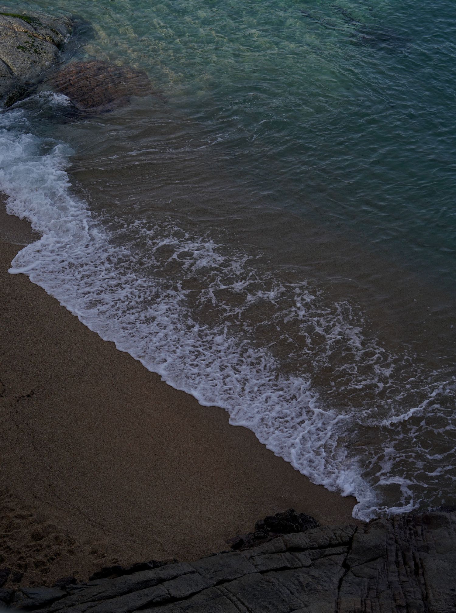 Crystal clear turquoise waves rolling onto a pristine sandy beach surrounded by rocky cliffs.