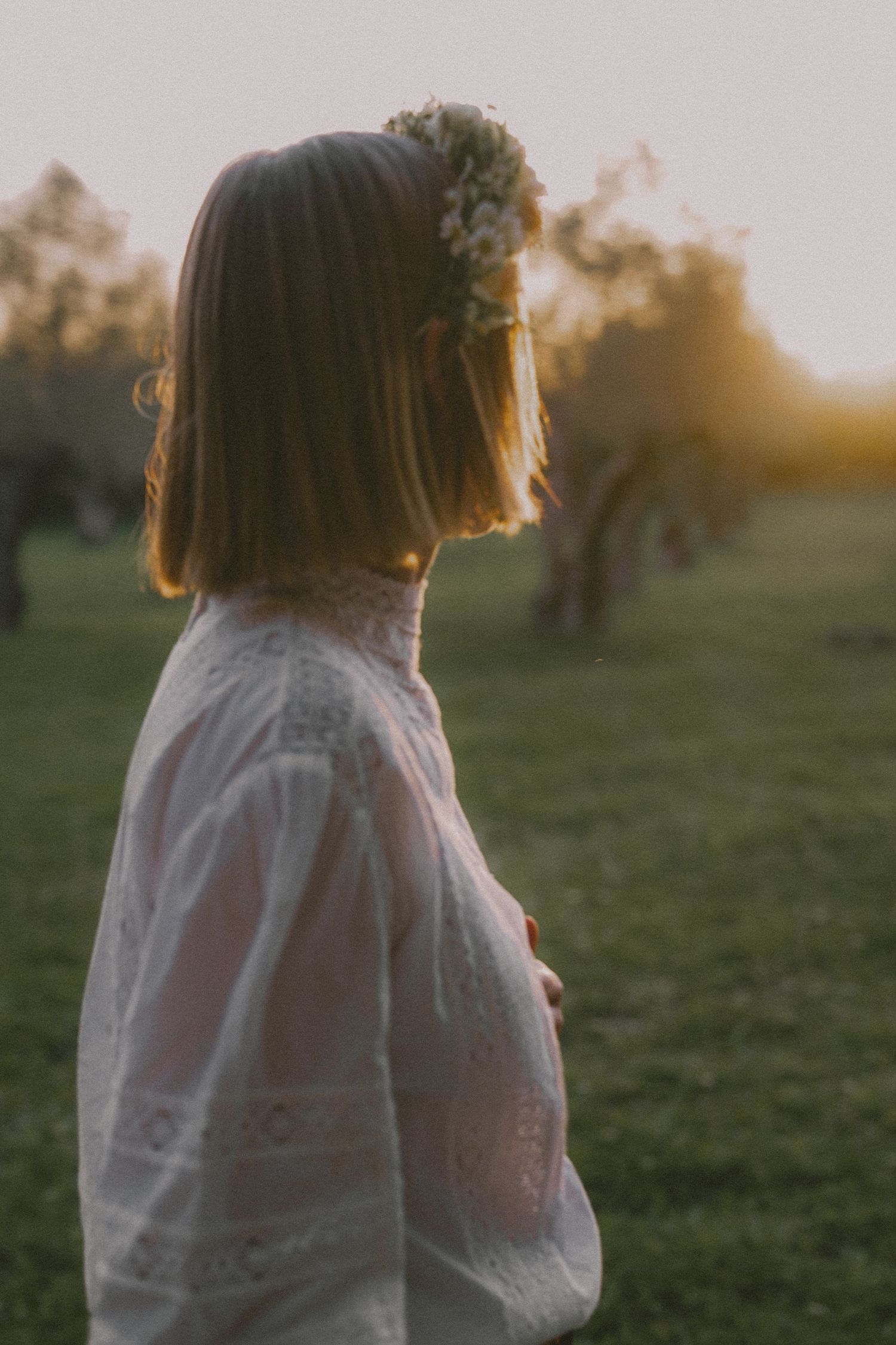 Silhouette in white dress against sunset in grassy field with golden light.