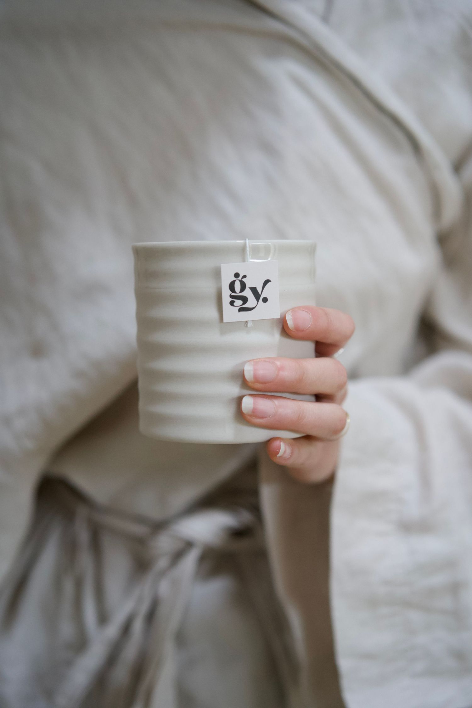 Hands holding a white ribbed ceramic mug with a small logo against a light gray background.