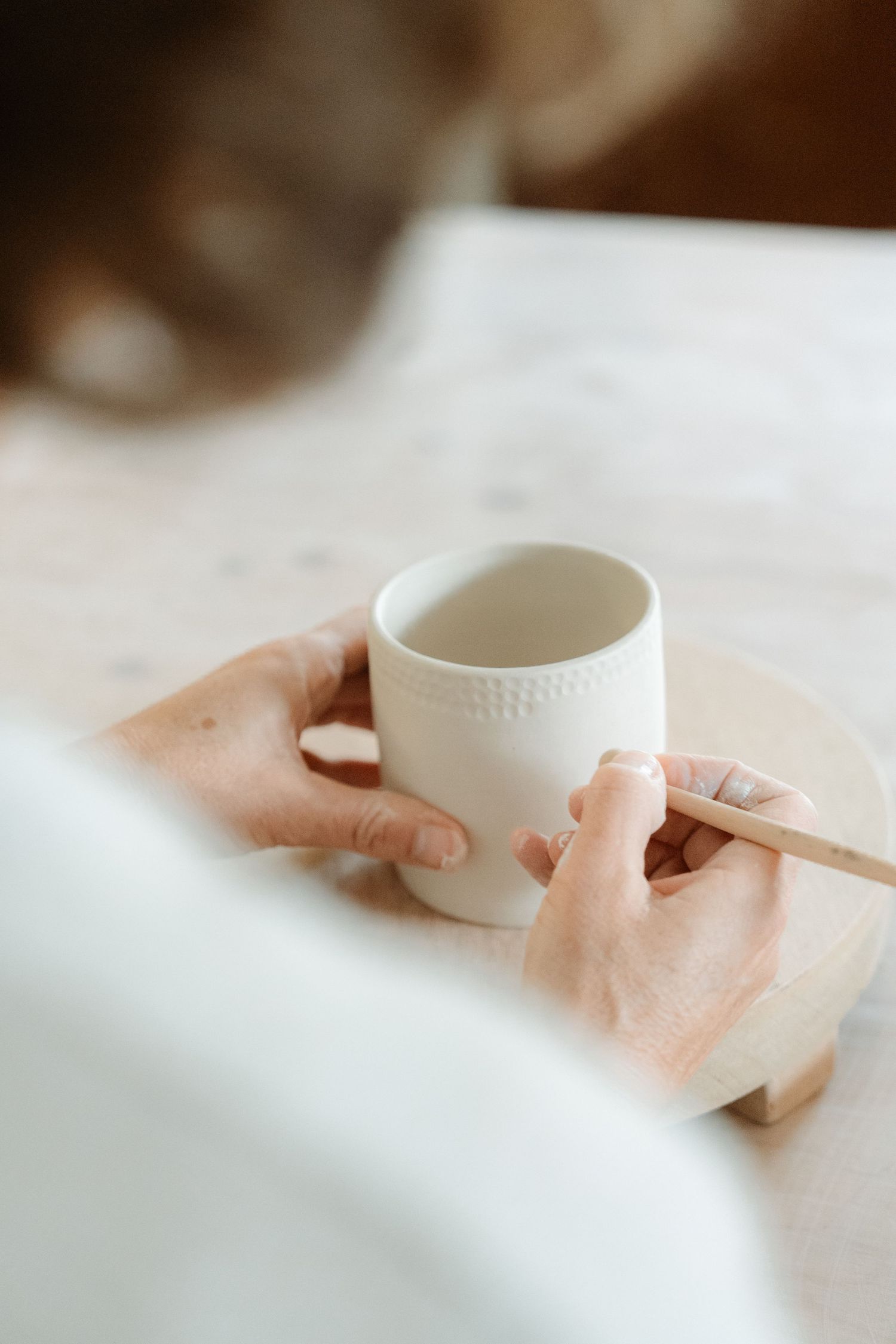 Hands carefully holding and examining a handcrafted white ceramic vessel.