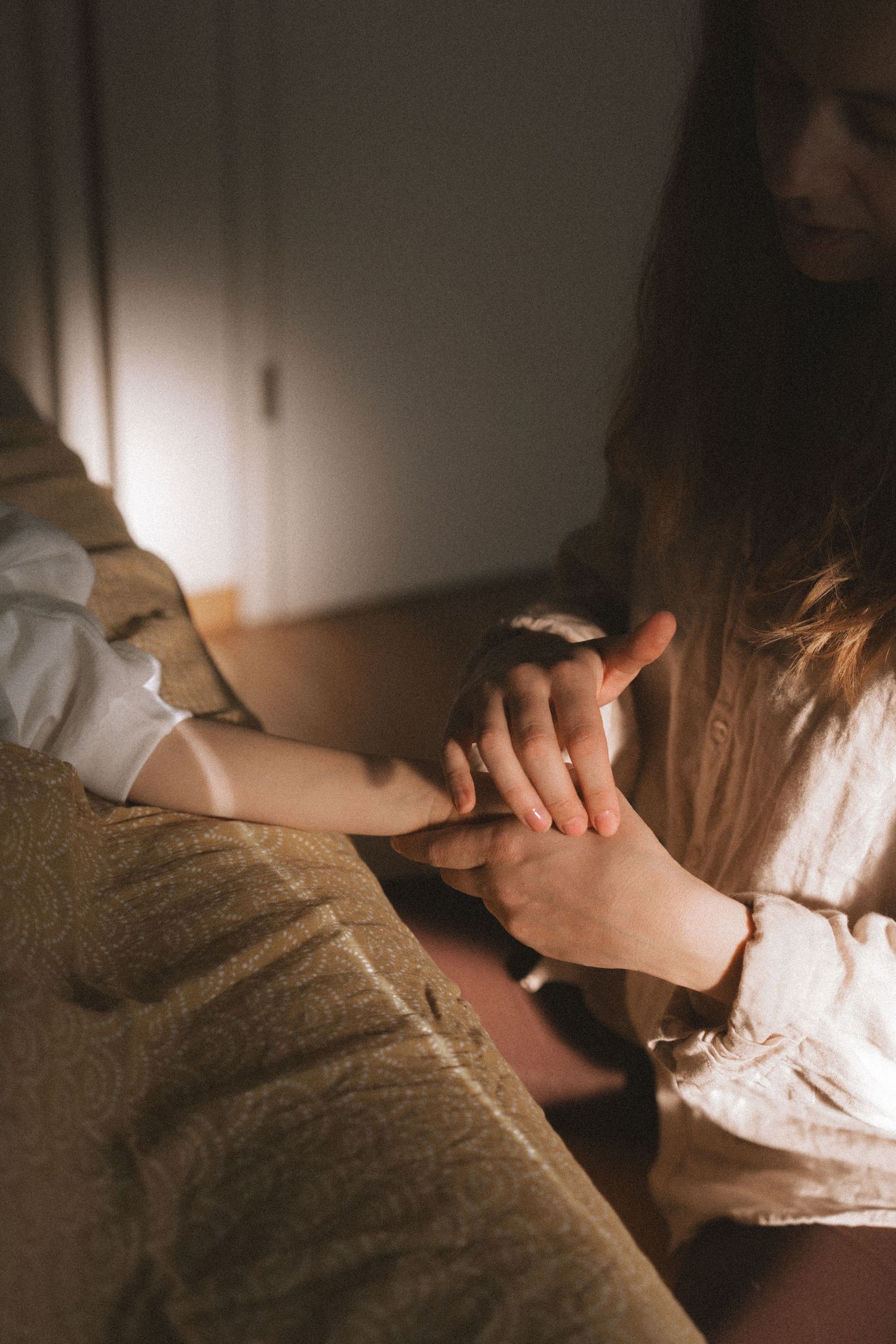 Hands delicately placed on textured bedding with dramatic shadows and soft lighting.