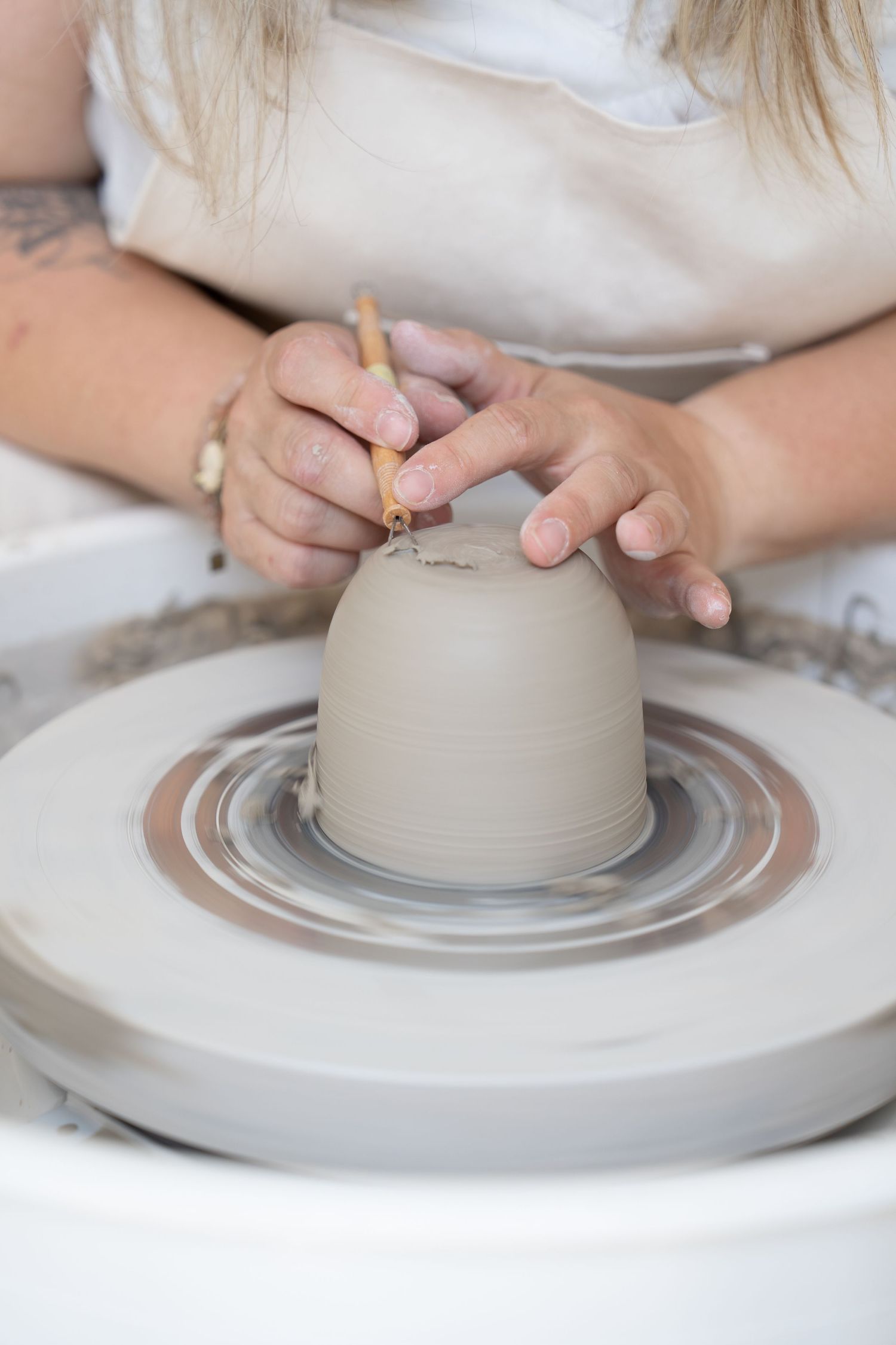Hands carefully sculpting a small clay vessel on a pottery wheel.