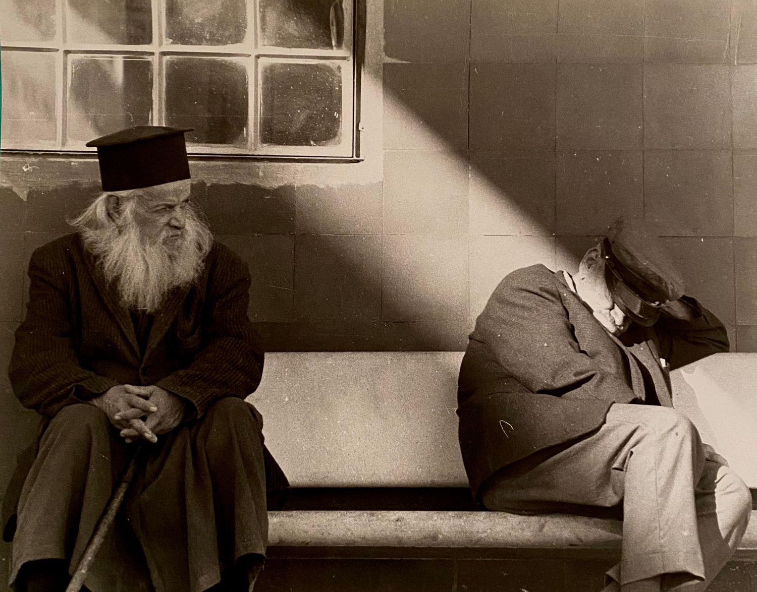 A sepia-toned vintage photograph shows a figure seated in a chair against a wall with dramatic lighting and shadows.