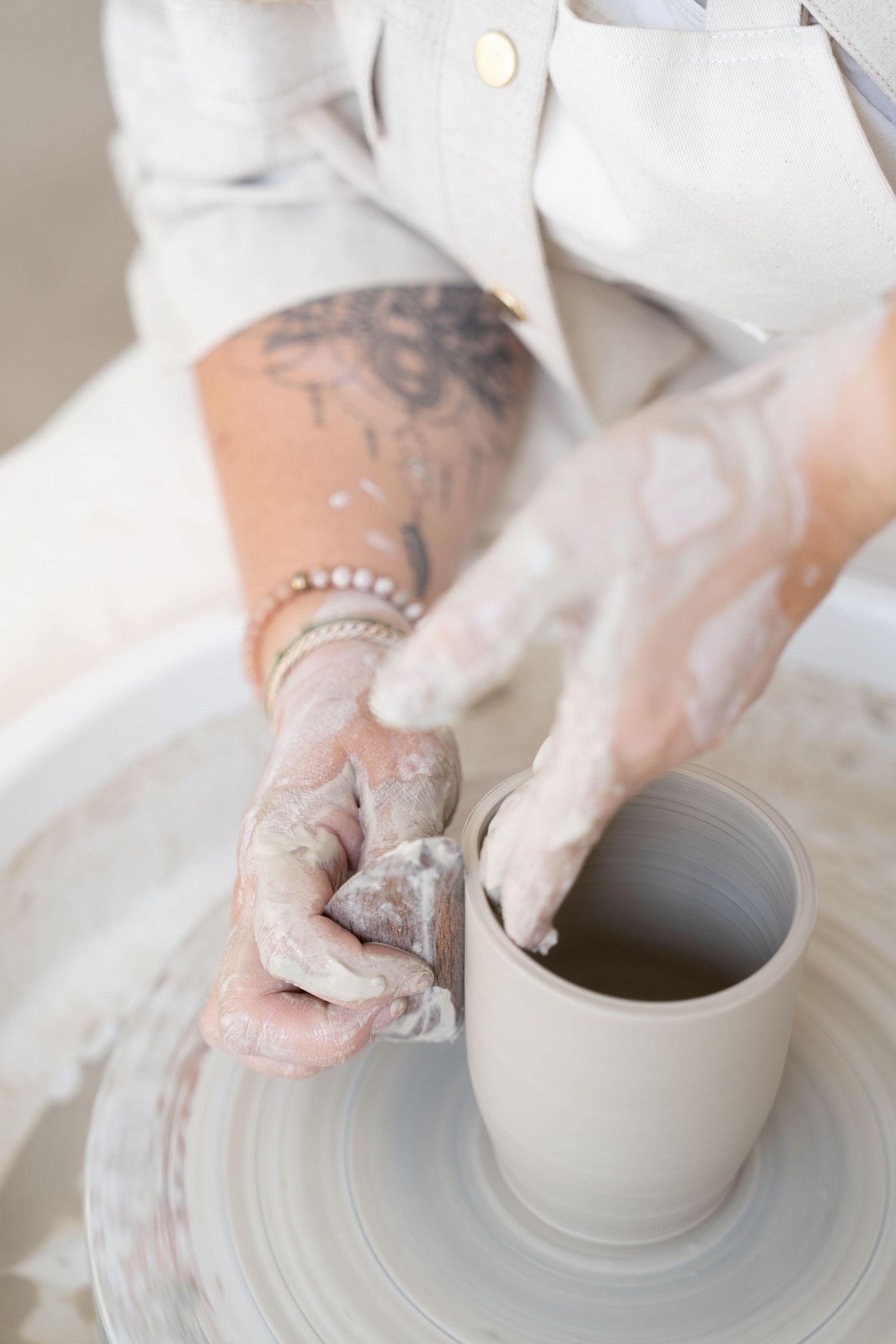 Hands working wet clay on a pottery wheel to shape a cylindrical form.