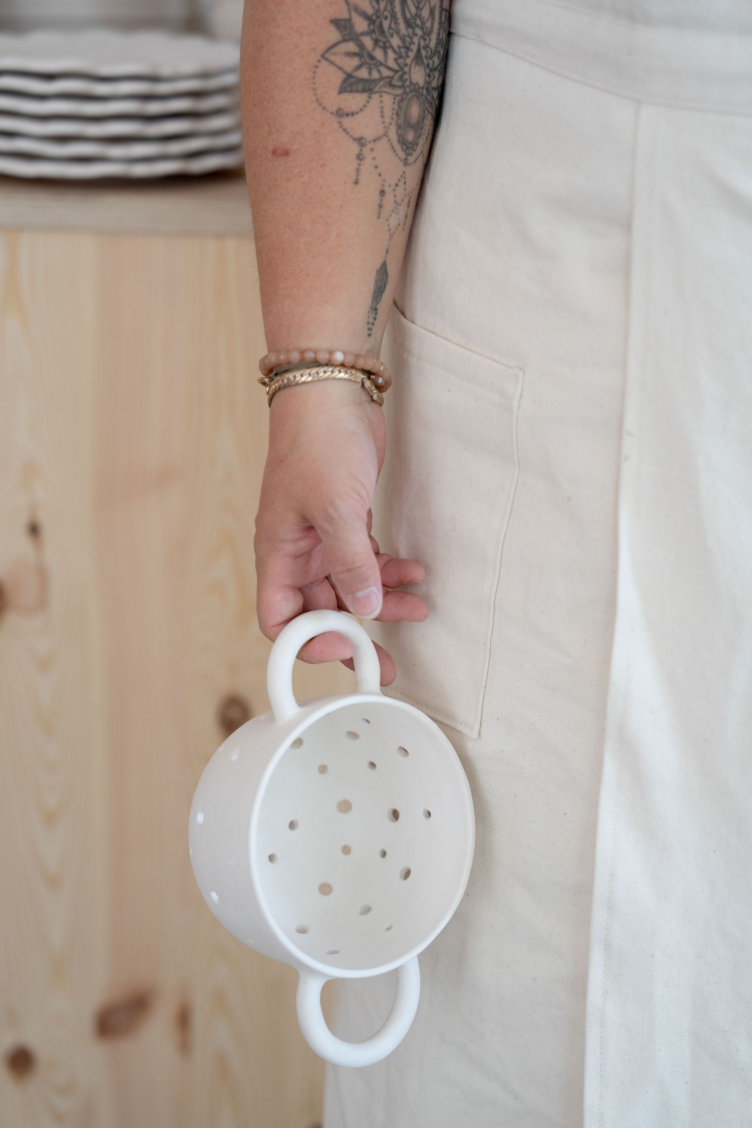 Hand holding a white ceramic colander with decorative hole pattern.