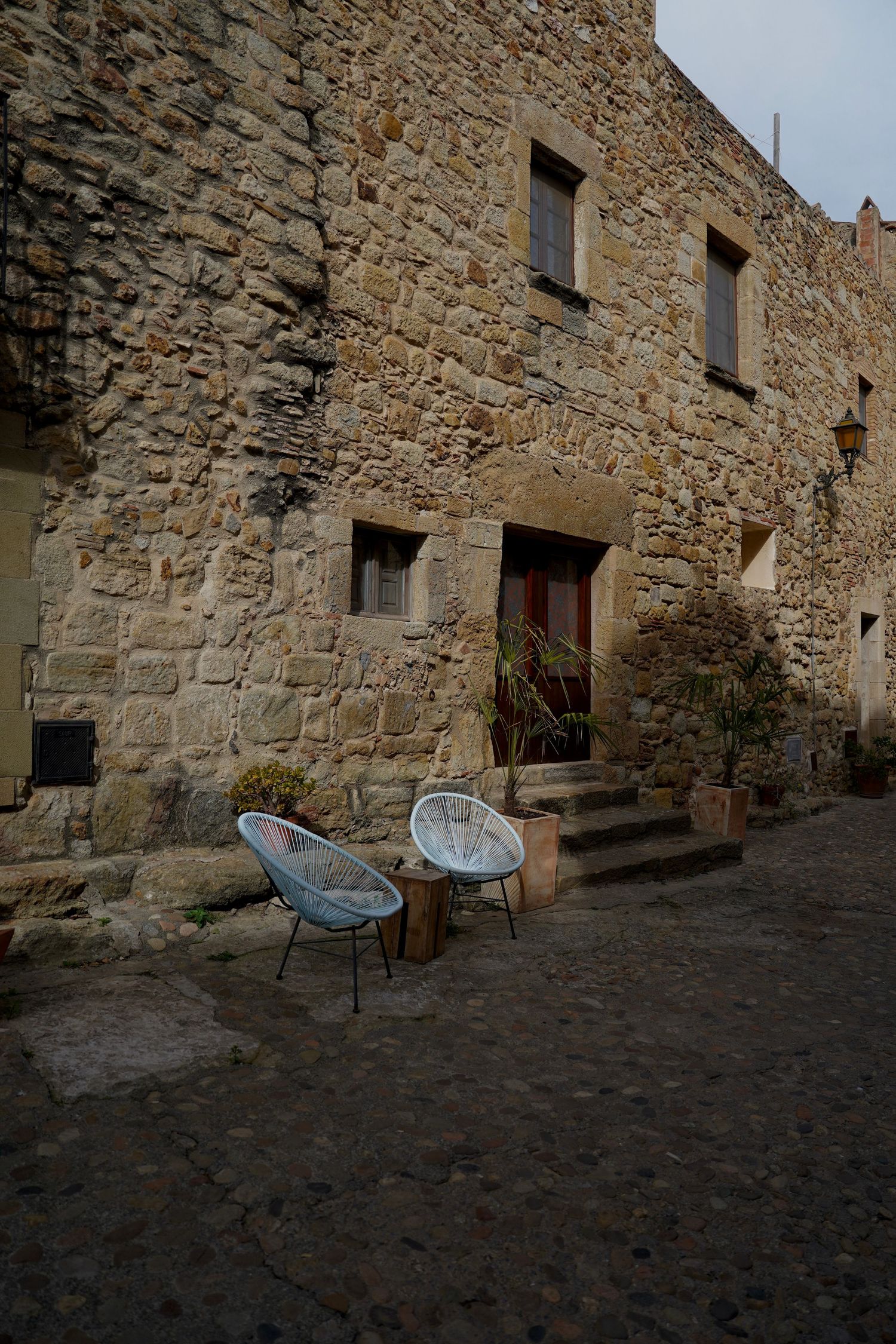 Historic stone wall buildings with modern patio chairs along a quiet village street.