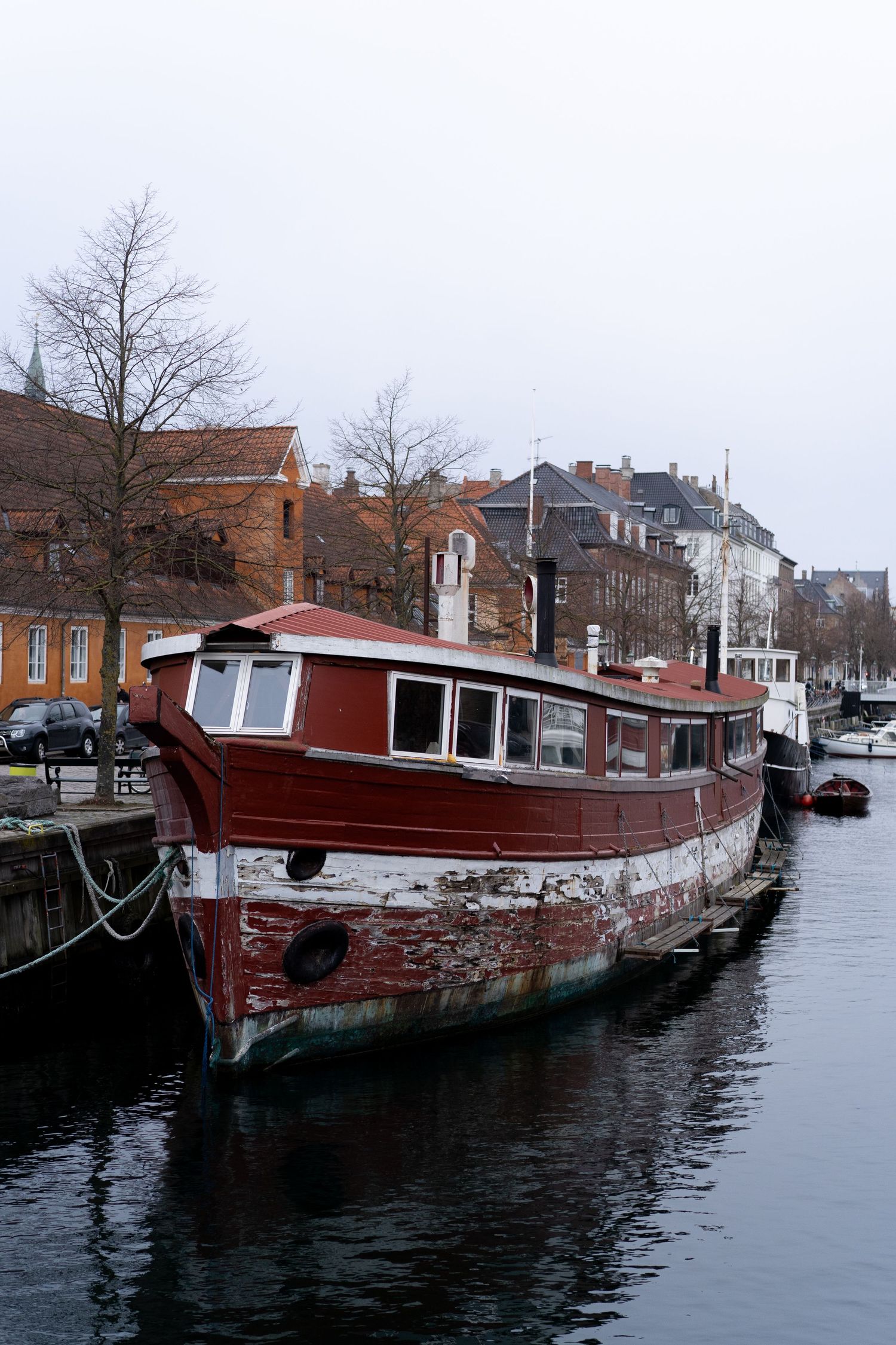 Red vintage houseboats moored in an urban canal with buildings in the background.