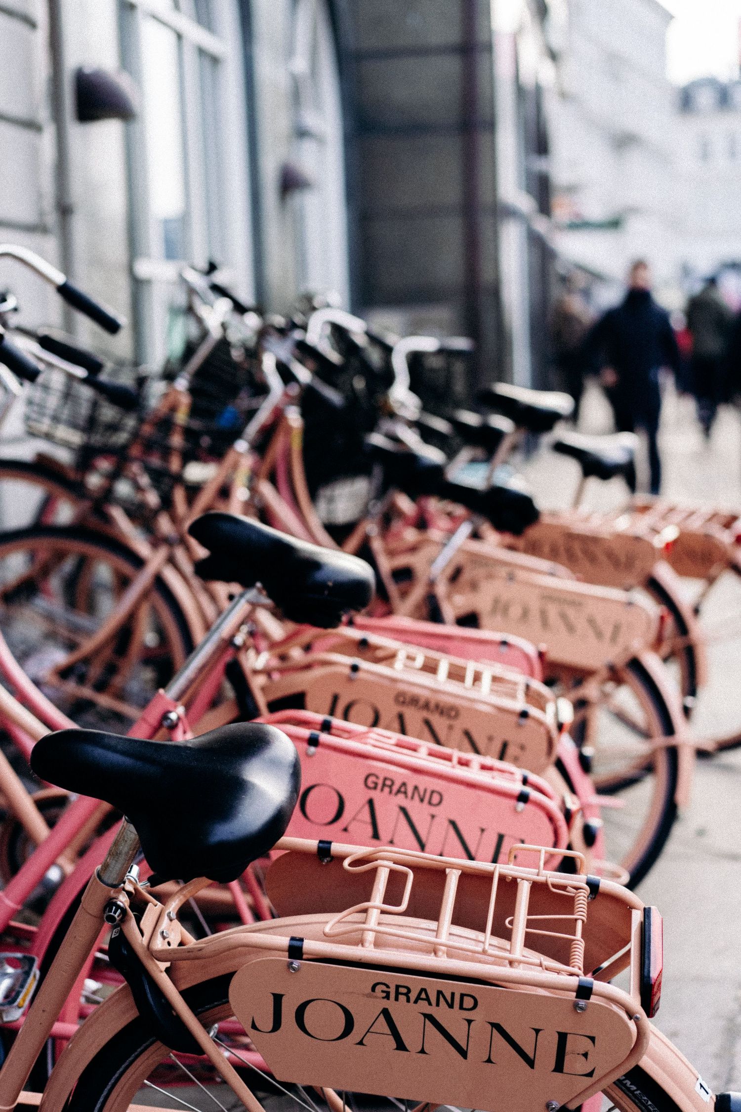 Row of pink rental bicycles with 'JOANNE' branding lined up on city street.