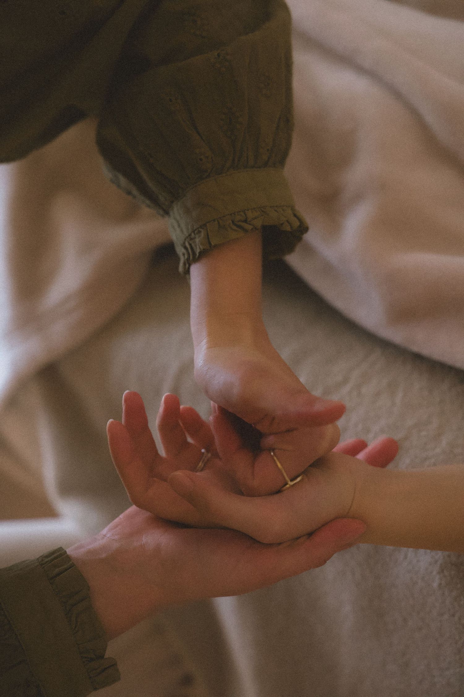 Close-up of hands in gentle contemplative poses against soft fabric background.