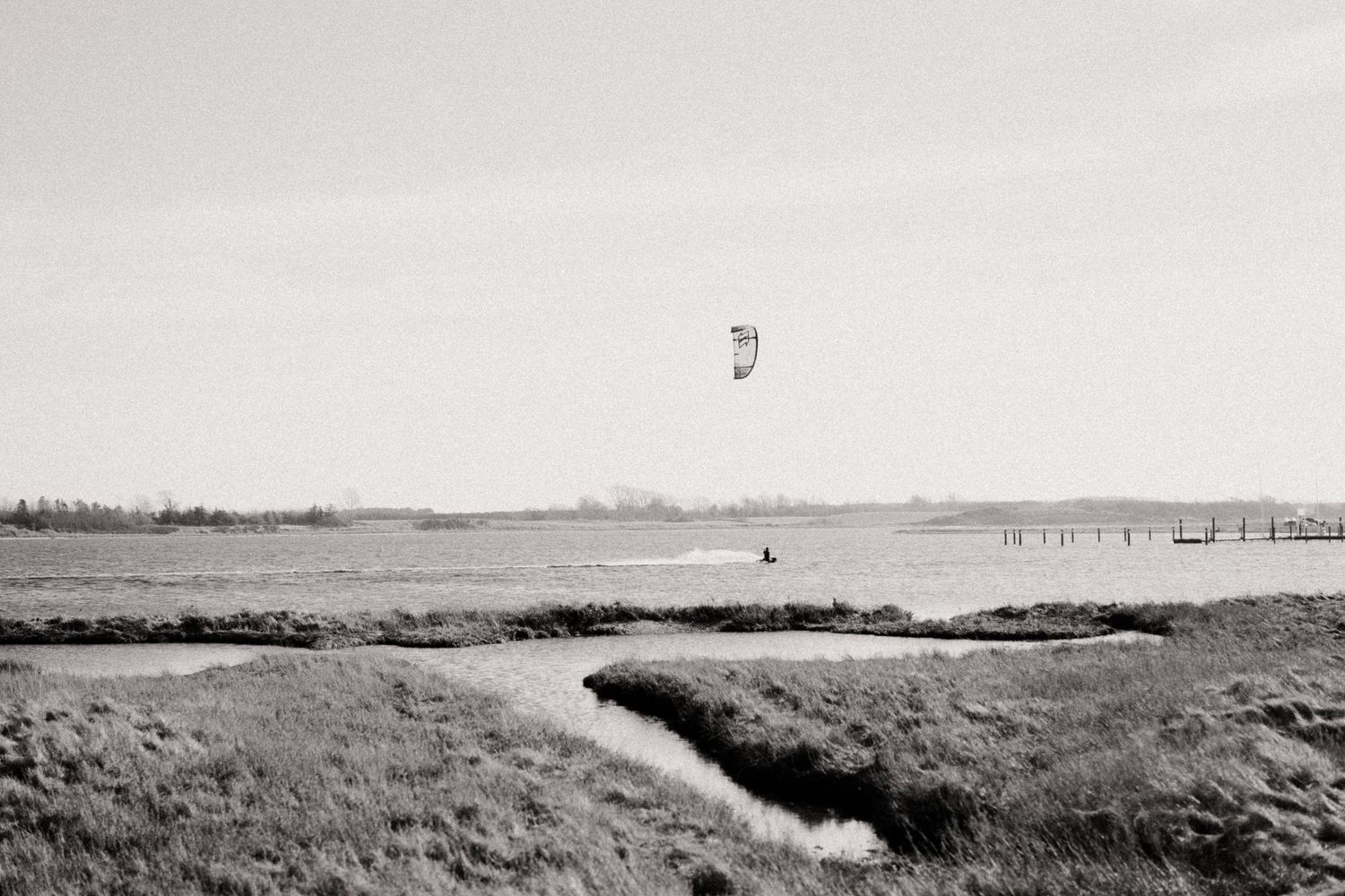 Minimalist landscape of flat marshland with distant structures on the horizon.