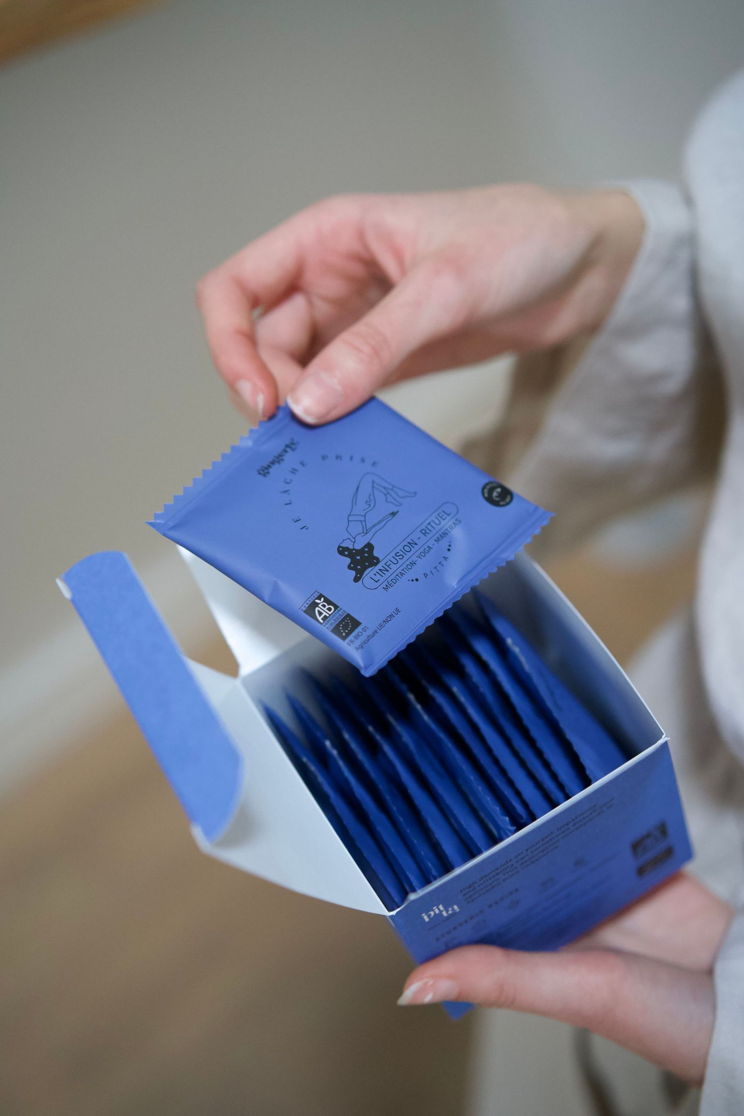 Opening a blue box of tea bags showing individual sachets inside.