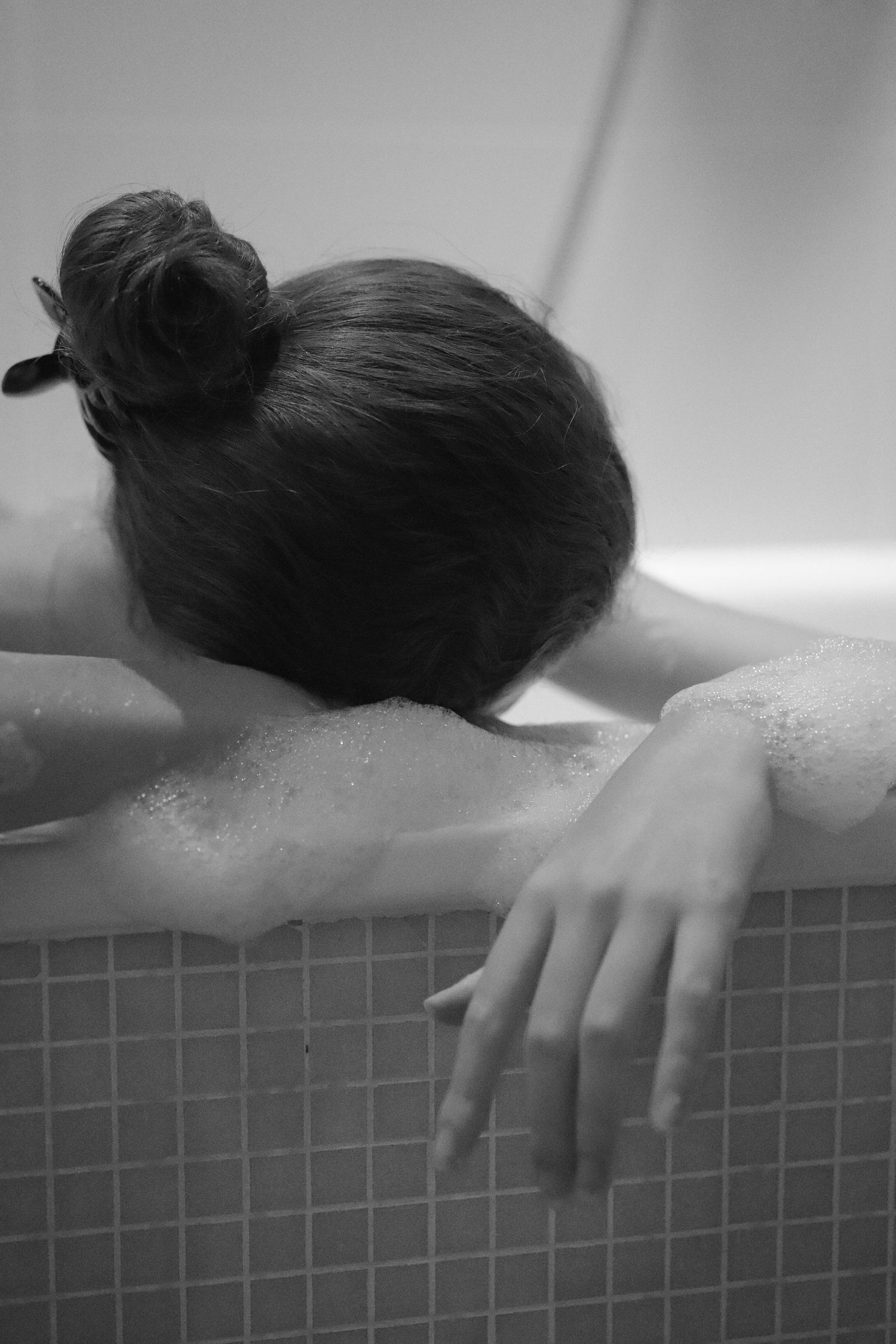 Hand resting on edge of bathtub with soap bubbles.