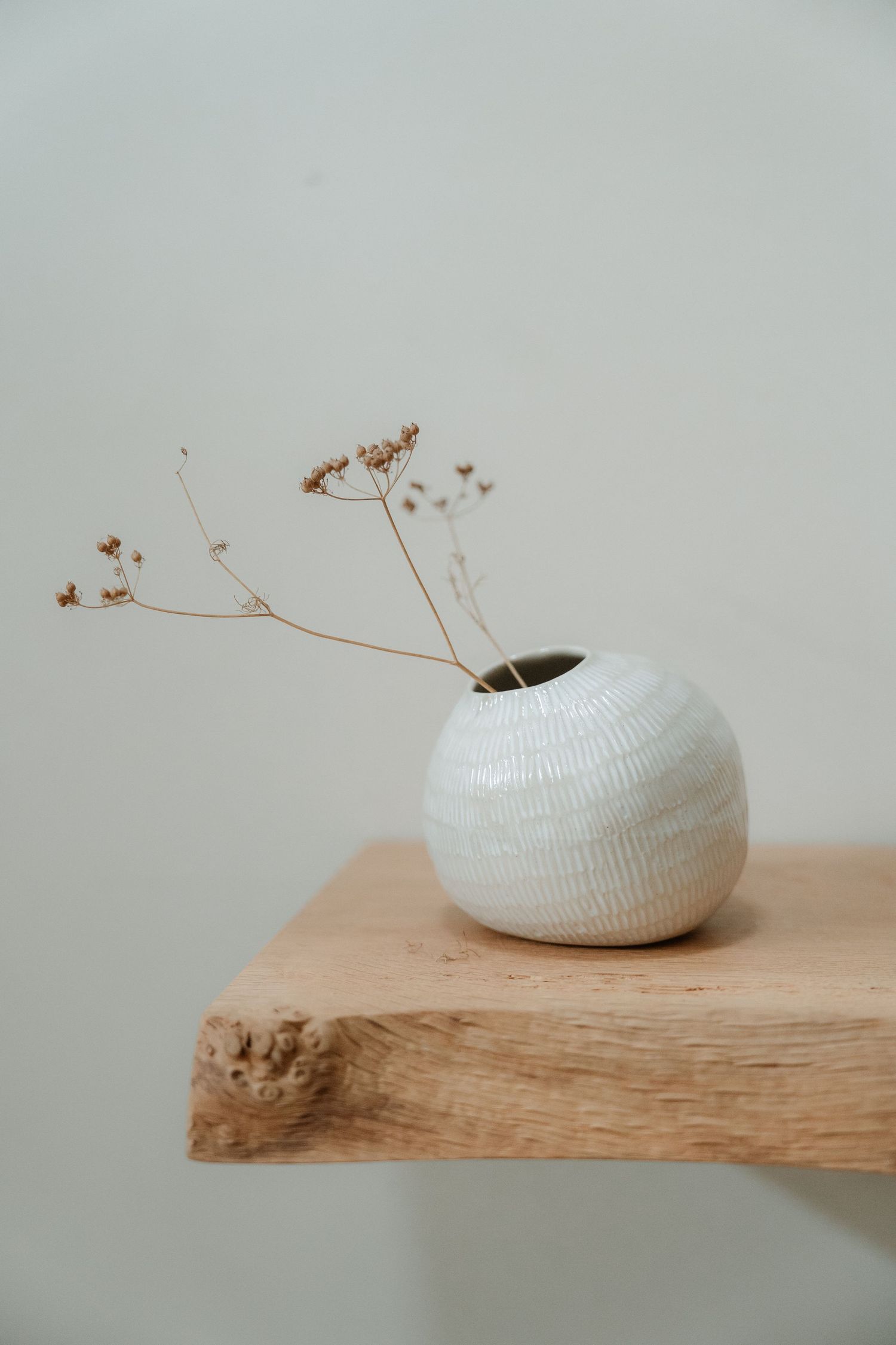 White ceramic bowl displayed on rustic wooden surface with delicate dried flowers.