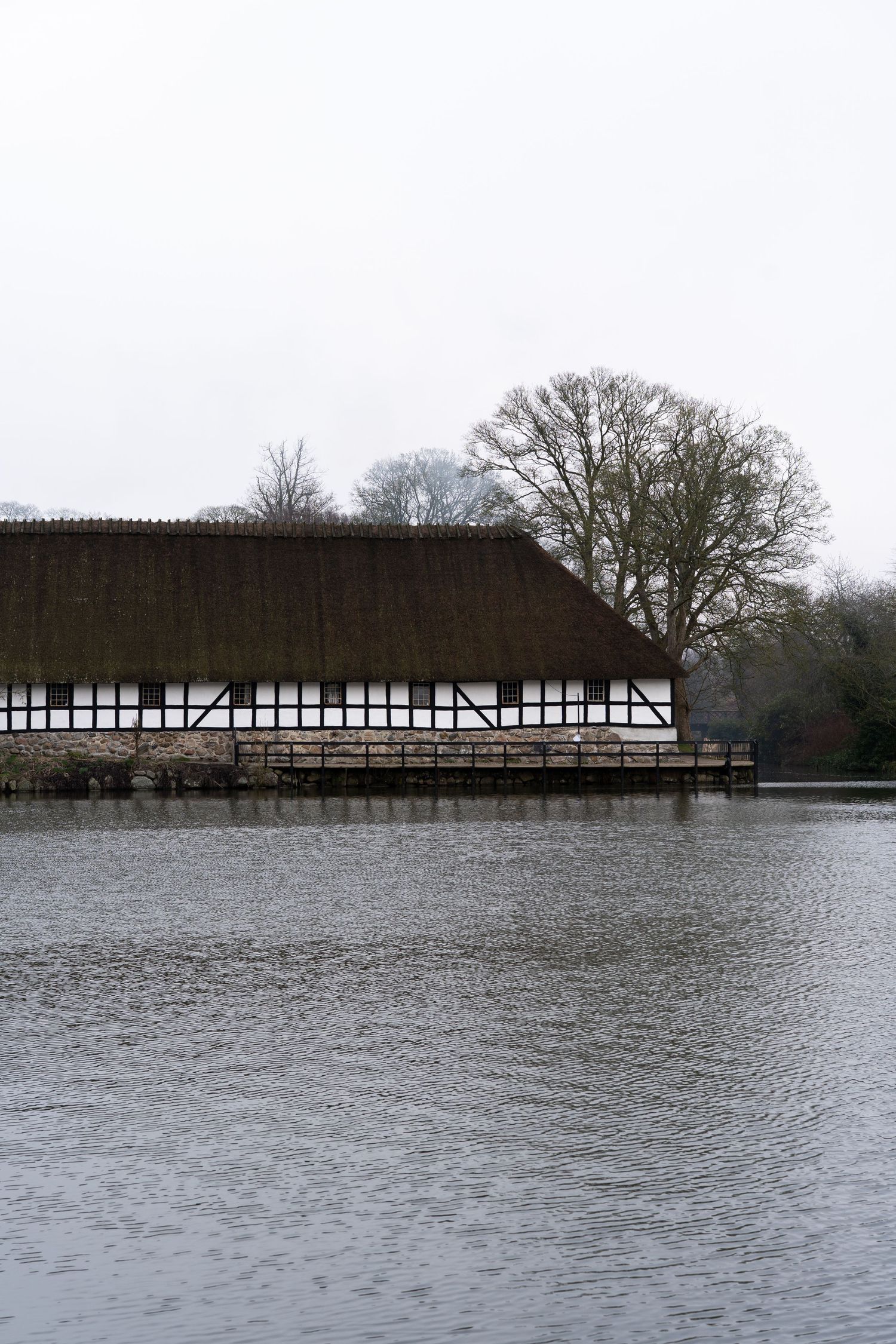 Long timber-framed building reflected in still lake waters during winter.