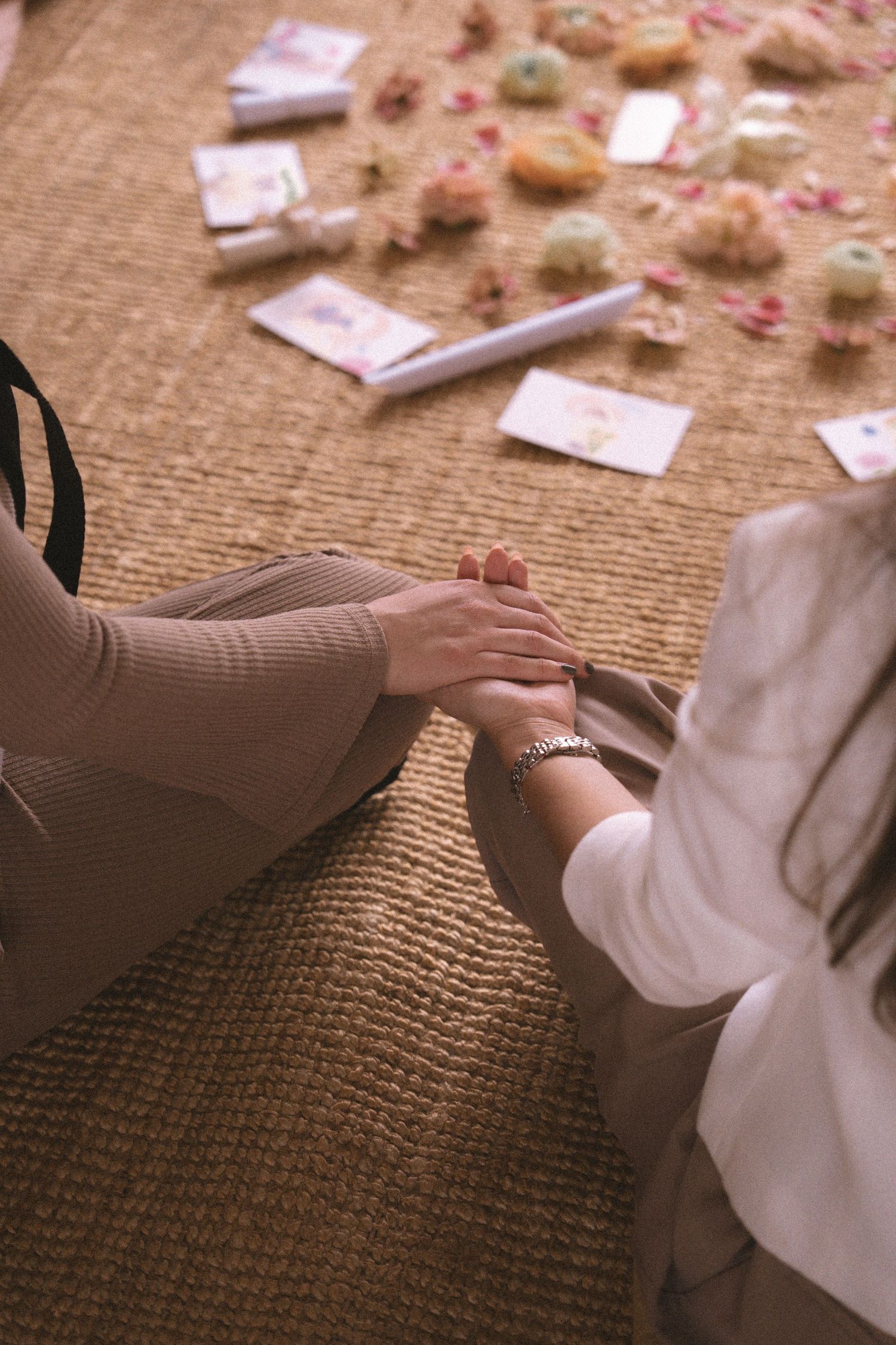 Hands reaching for scattered tarot cards and rose petals on a textured burlap surface.