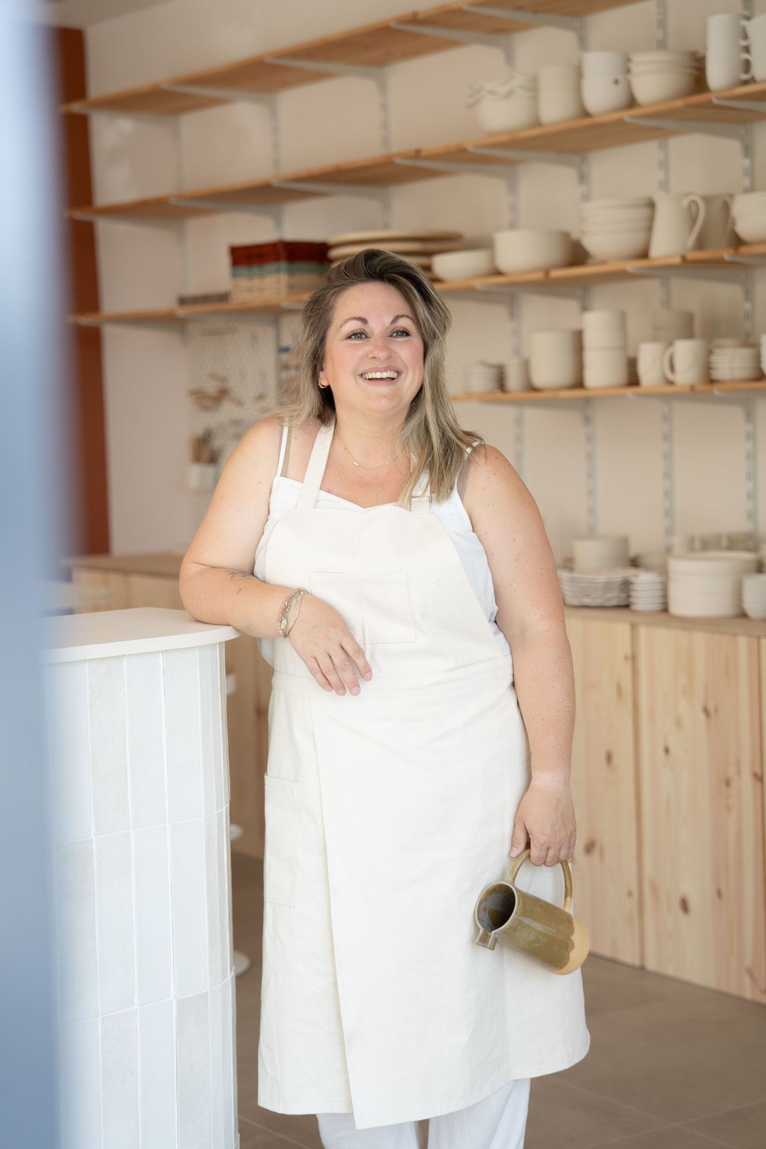 Bright pottery studio with wooden shelving displaying white ceramic pieces.