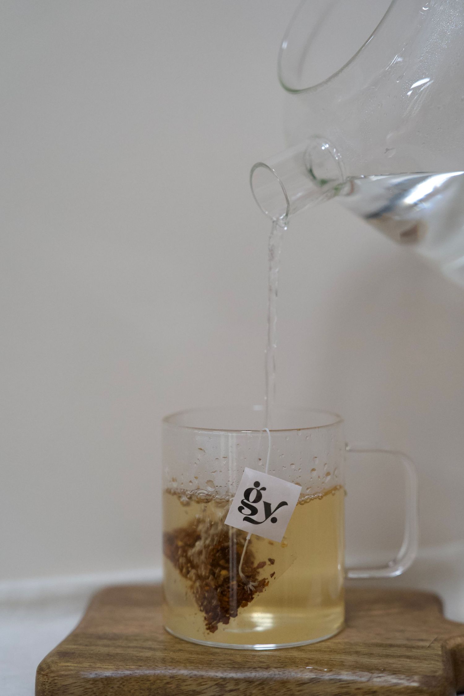 Pouring hot water into a clear glass mug with tea bag on wooden surface.