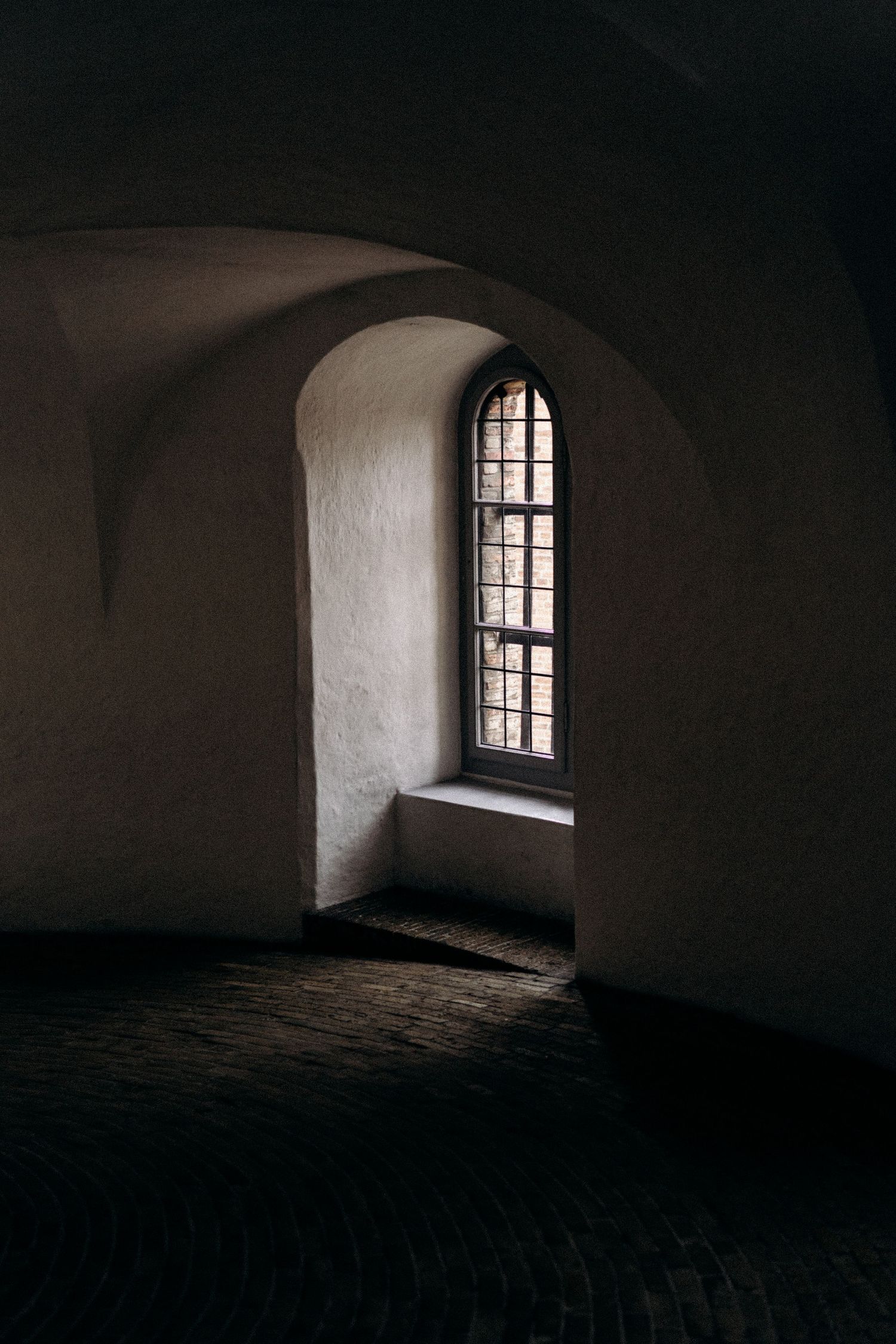 Dark interior with a single arched window casting light into a minimalist stone room.