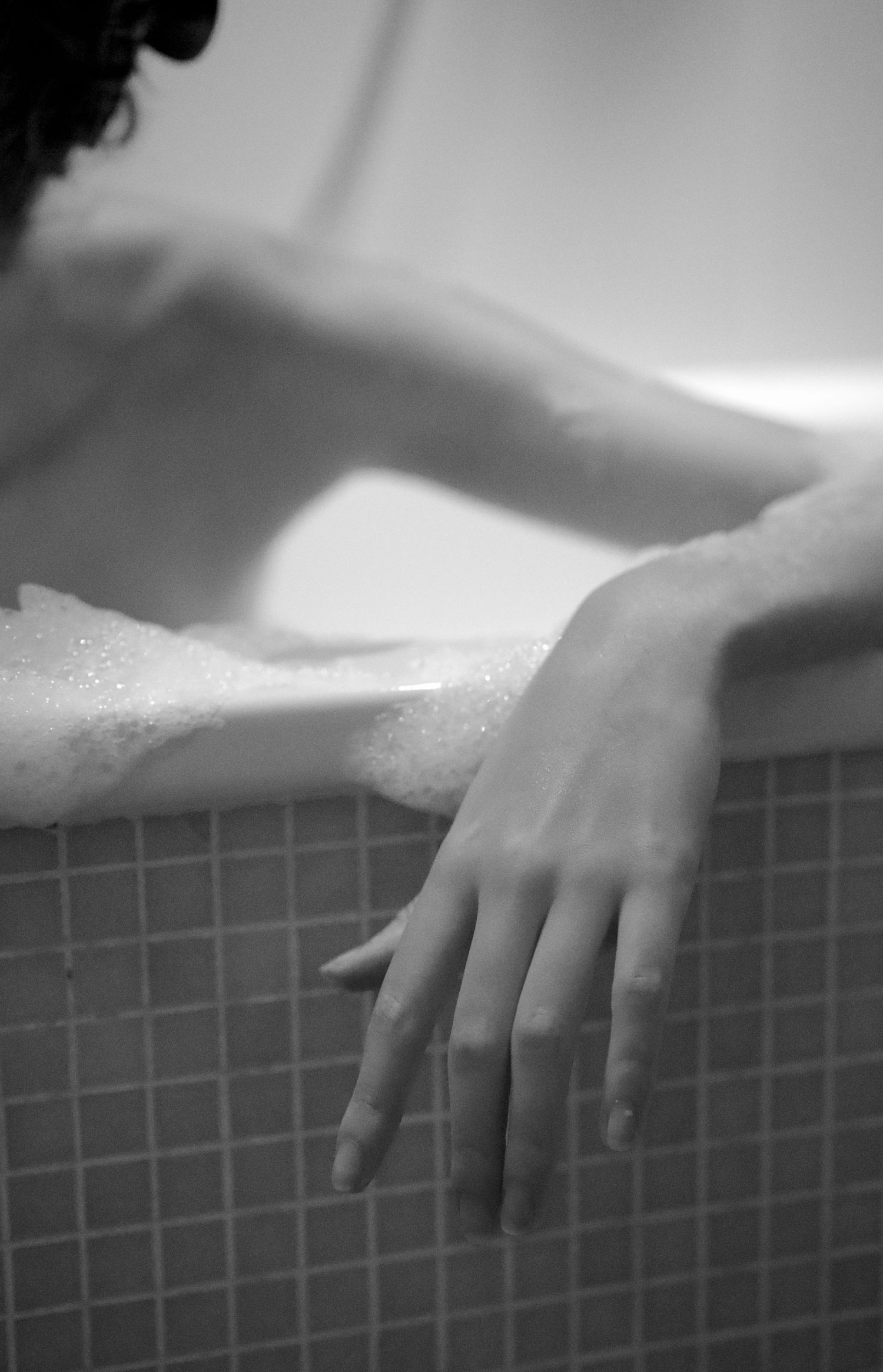 A hand resting on the edge of a bathtub filled with soapy bubbles.
