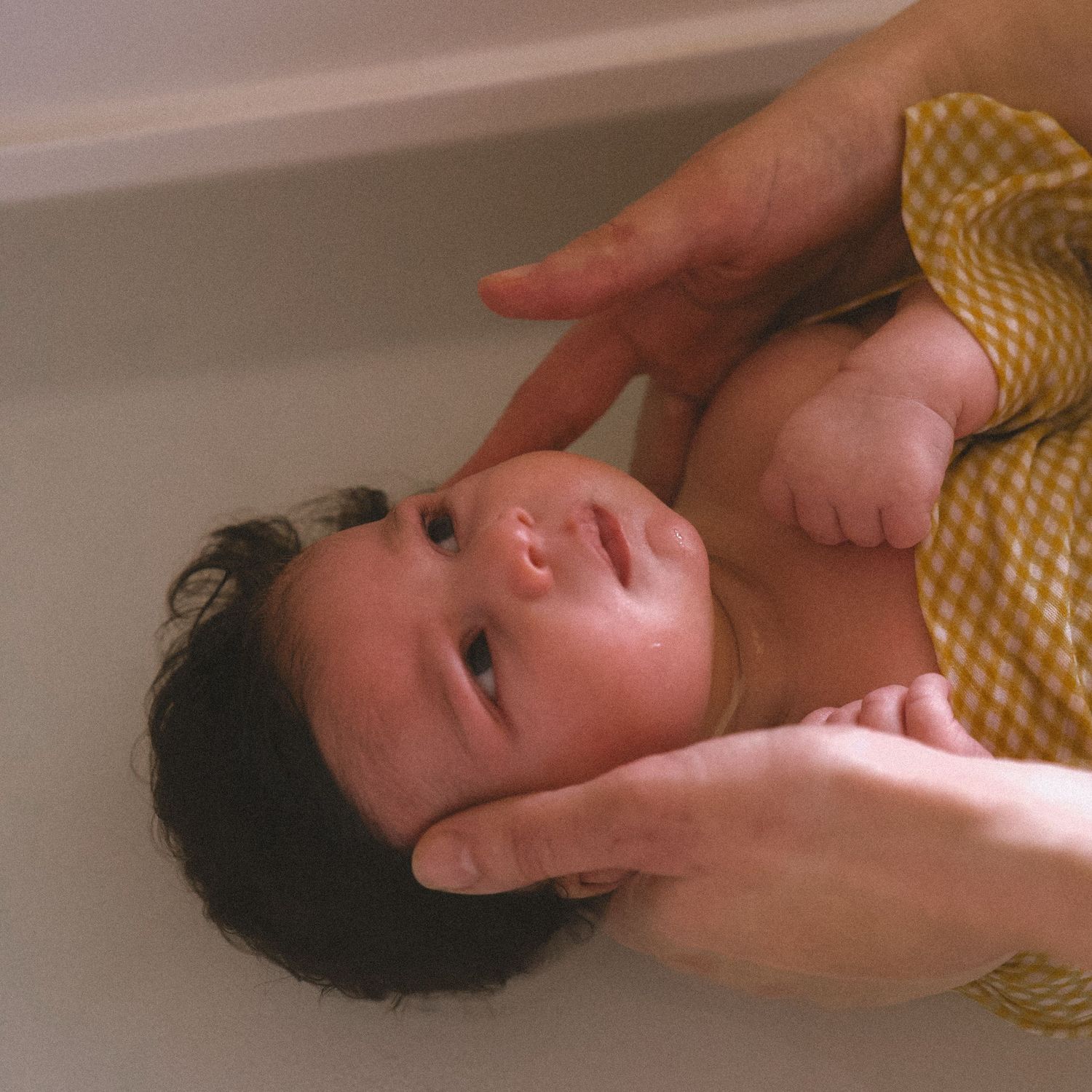 A person soaking in a bathtub while hands reach down to touch the water's surface.