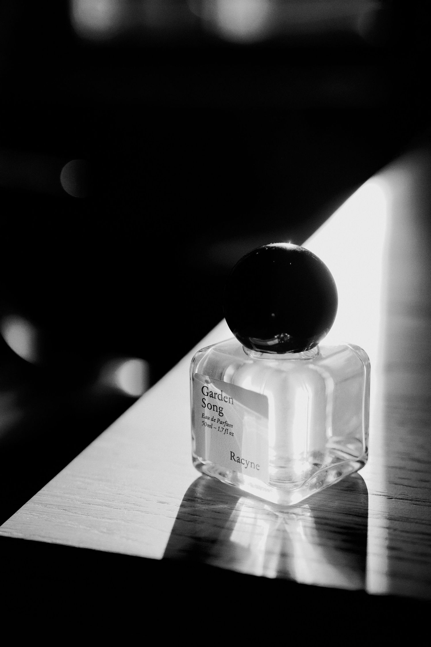 Black and white abstract photography of a perfume casting dramatic shadows on a reflective surface.