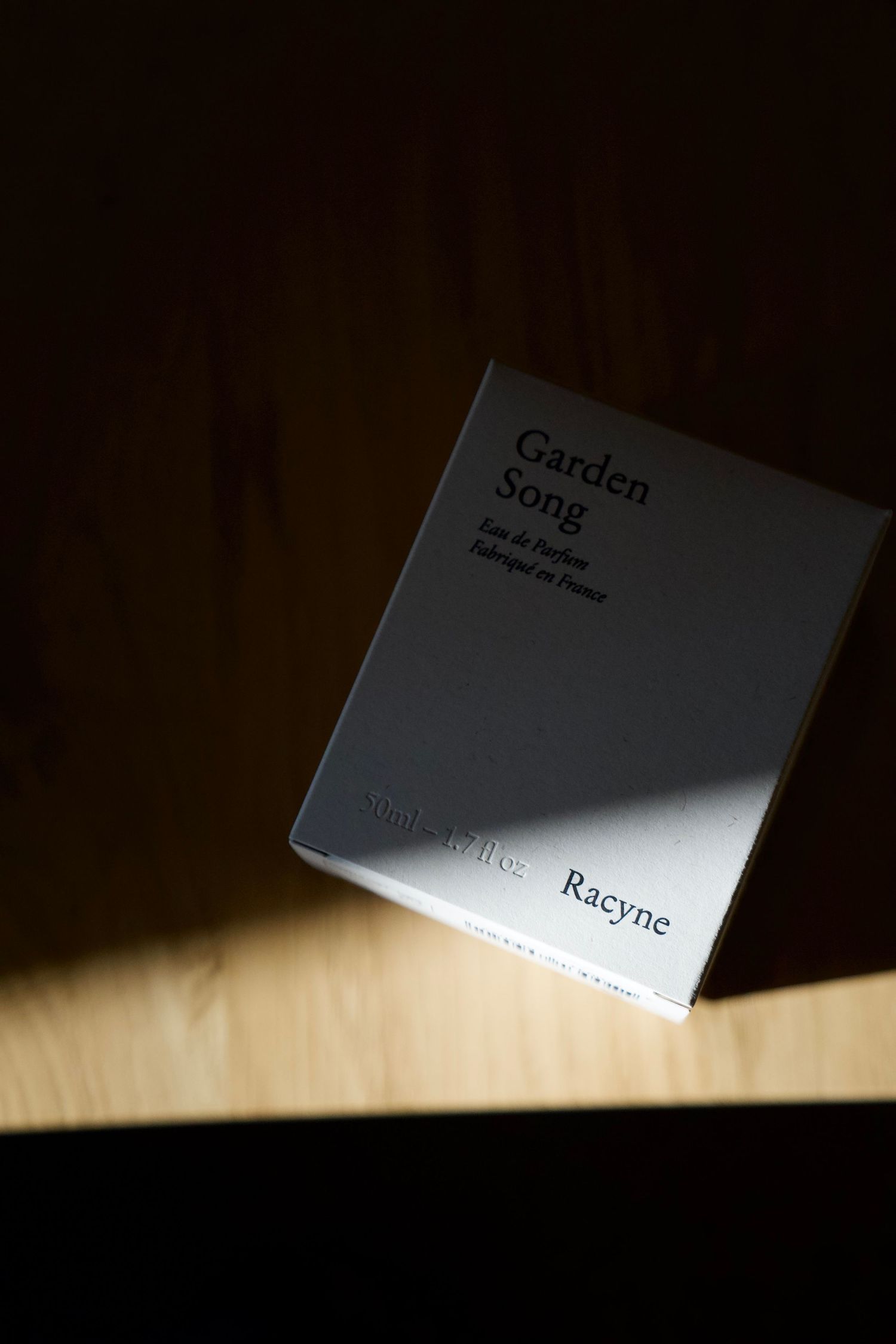 White perfume box floating in dramatic lighting against dark background creates minimalist composition.