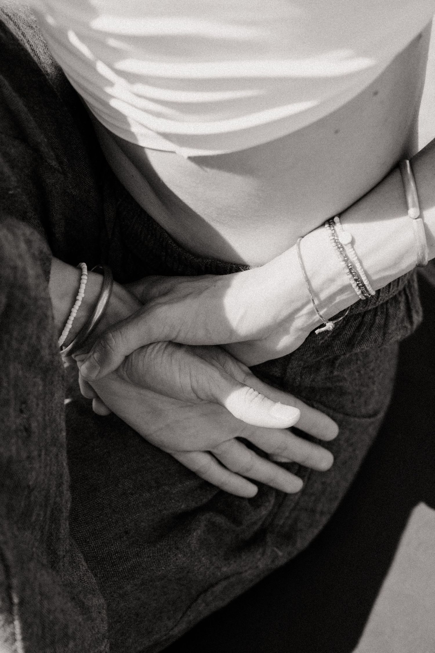 A sequence of black and white photos showing hands with bracelets resting on dark fabric.