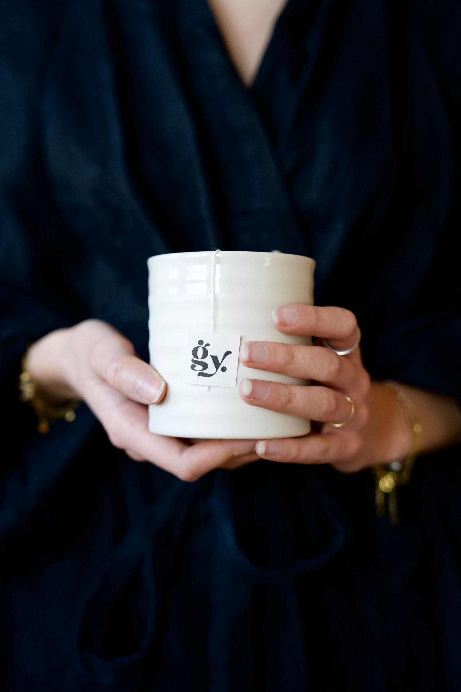 Hands holding a small white ceramic cup against a dark background.