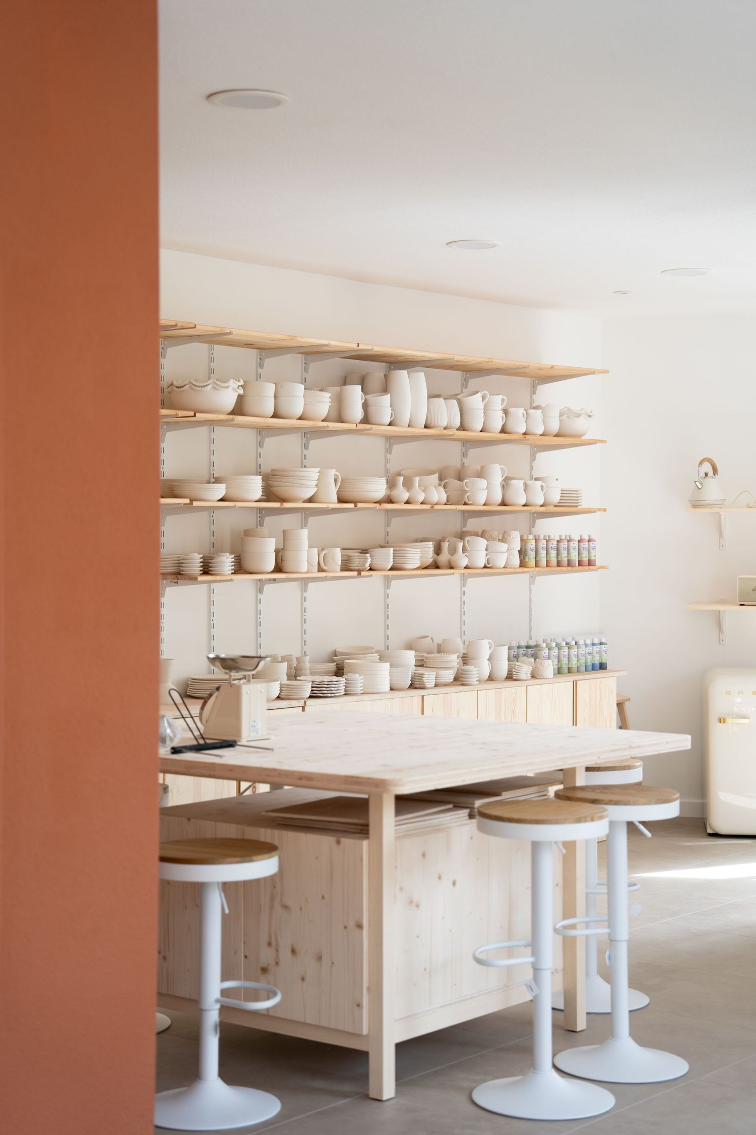 Clean pottery studio with white shelves displaying ceramic pieces and work tables.