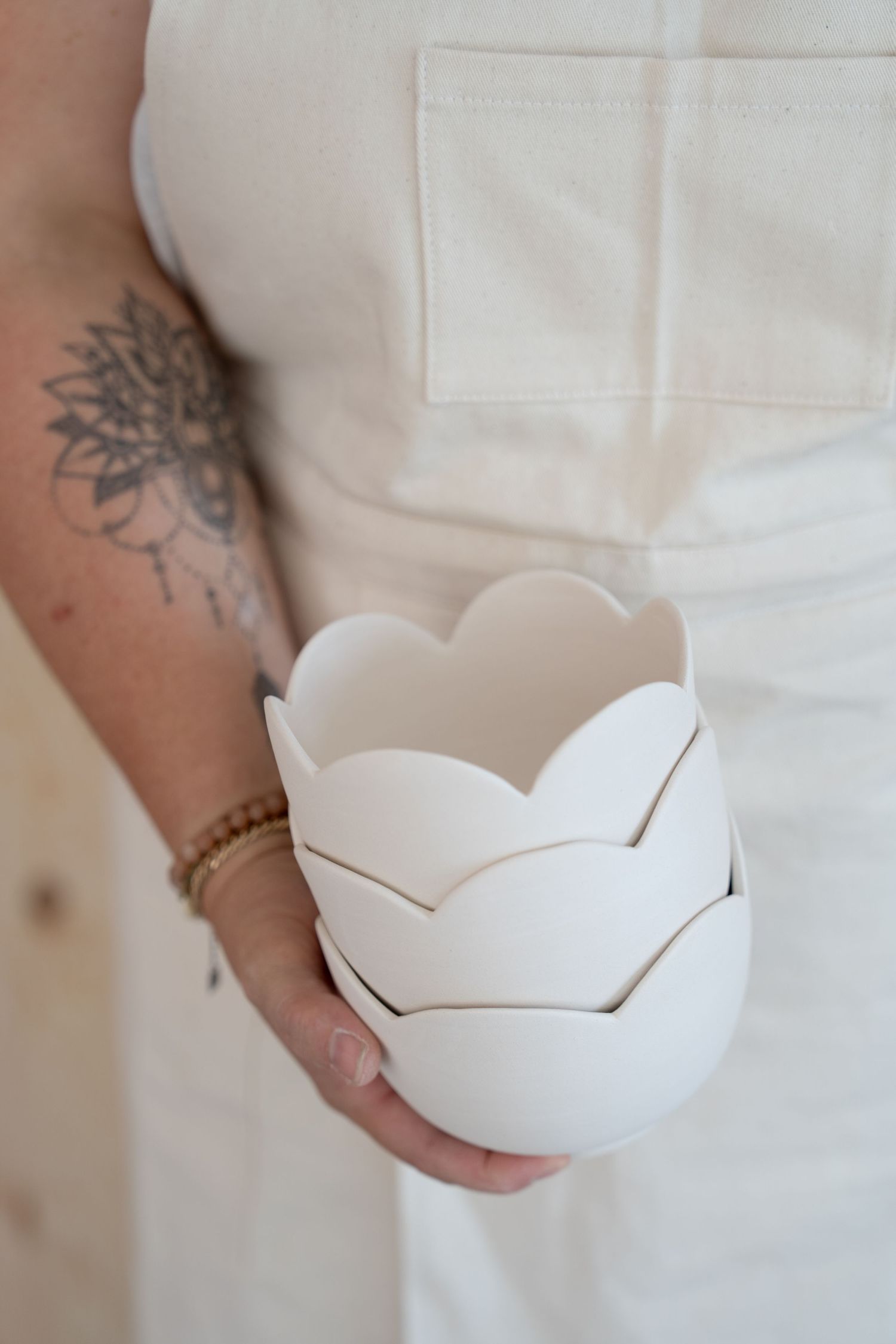 White ceramic bowl with petal-like edges being displayed against white apron.