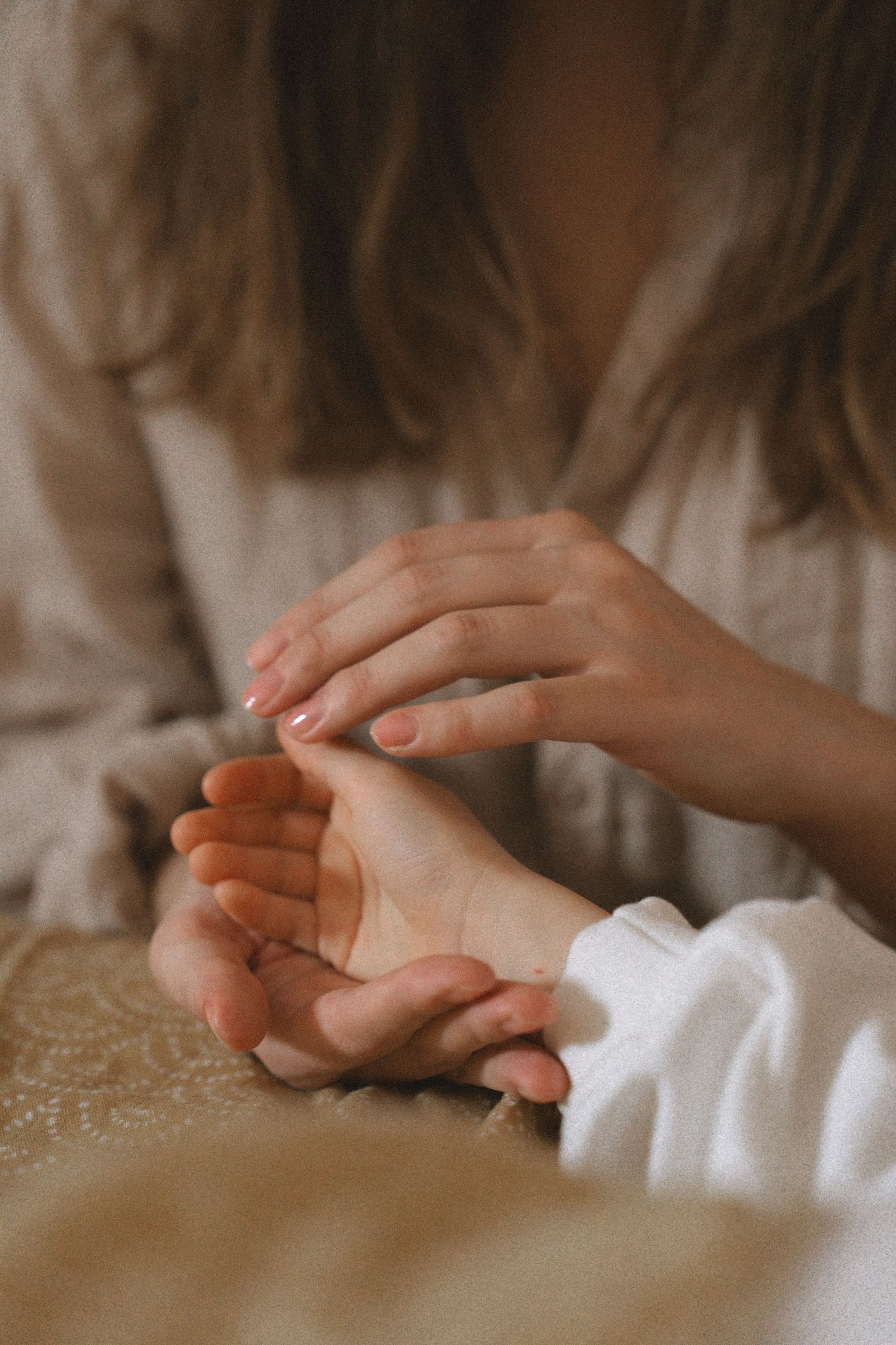 Close-up of hands gently resting on soft white fabric in warm natural lighting.