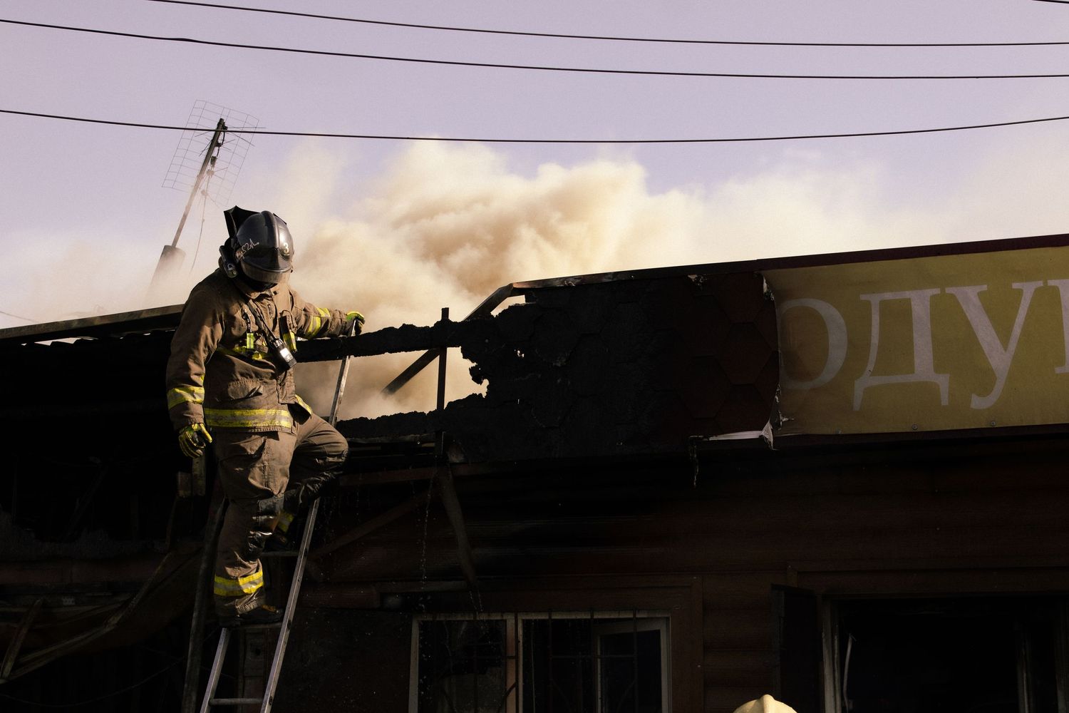 Firefighter on ladder working to extinguish building fire at dusk.