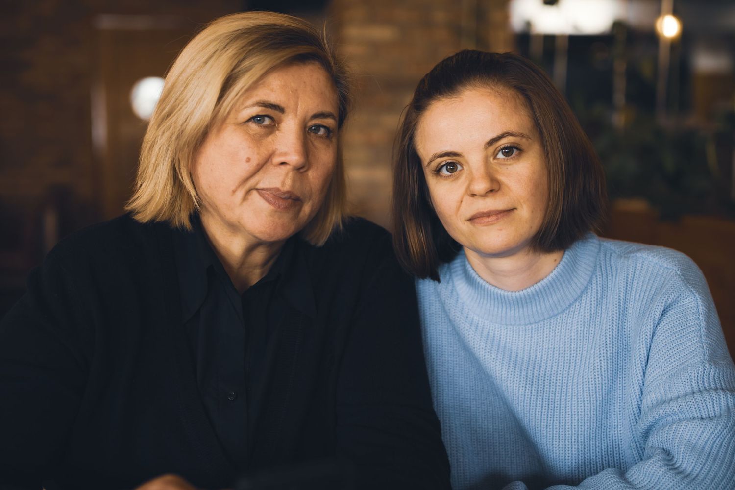 Two women in sweaters sharing an intimate moment in warm indoor lighting.