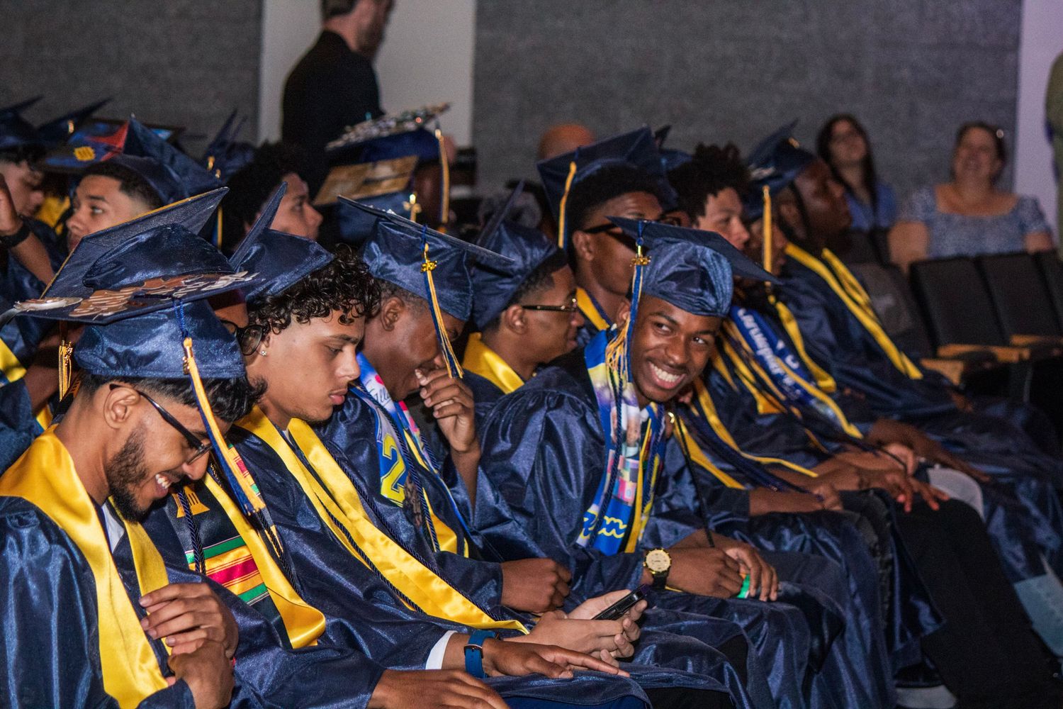 Graduates in blue and gold regalia seated during commencement ceremony.