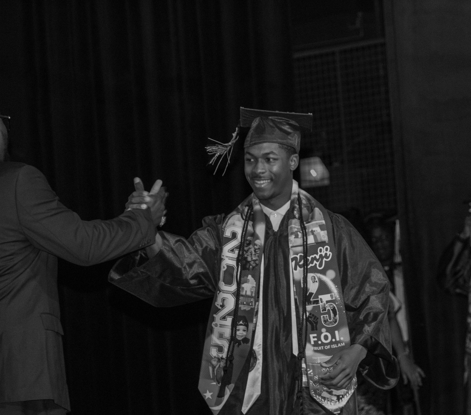 Graduate in cap and gown with decorated stole celebrating at graduation ceremony.