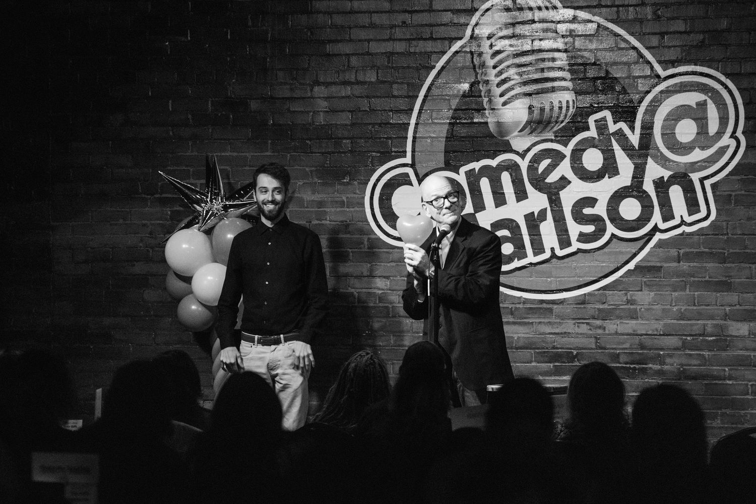 Black and white comedy club stage with microphone stand and logo.