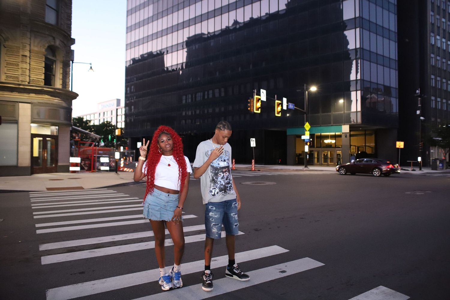 Urban street scene at dusk with tall glass buildings and crosswalks.