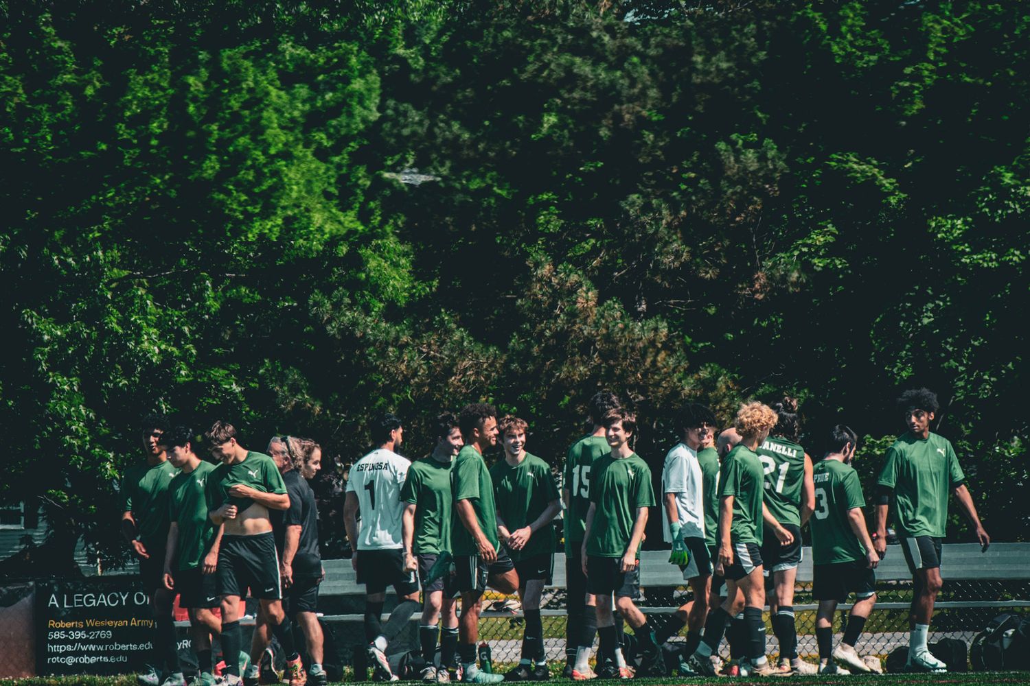 Soccer team in green jerseys gathering outdoors surrounded by lush trees.
